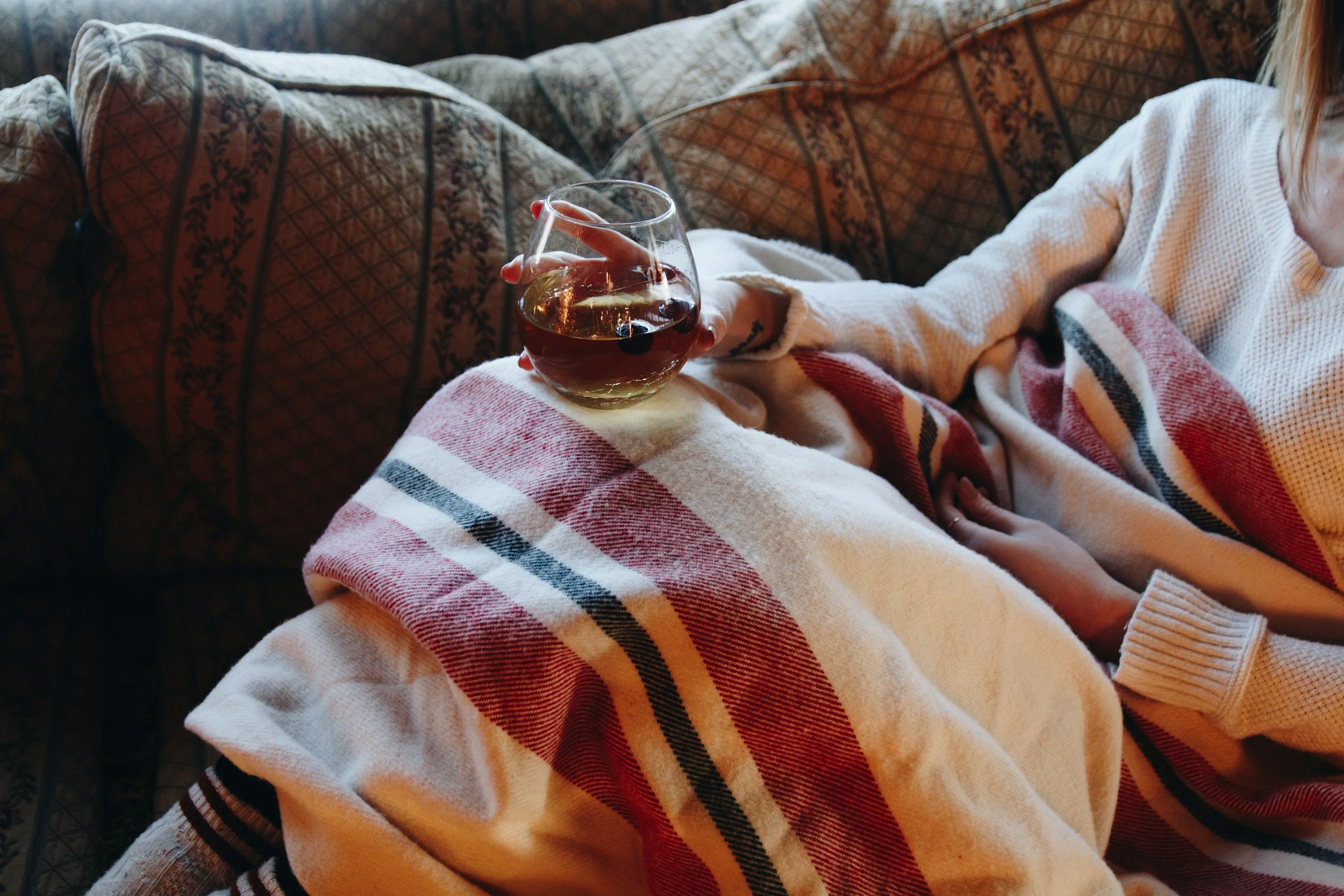 Woman relaxing on a couch under a blanket with a glass of wine in the evening, a habit that can affect sleep in perimenopause