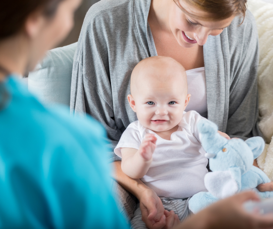A woman is holding her baby and they are both smiling. A postpartum doula is with them providing care, but you can only see her shoulder.