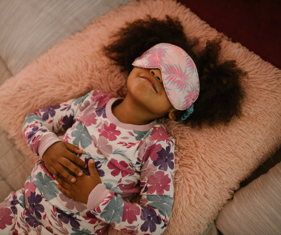 A young girl smiles softly with a sleep mask on, looking calm and settled at bedtime — the kind of peaceful sleep readiness that neurodivergent children can reach with the right foundations in place.