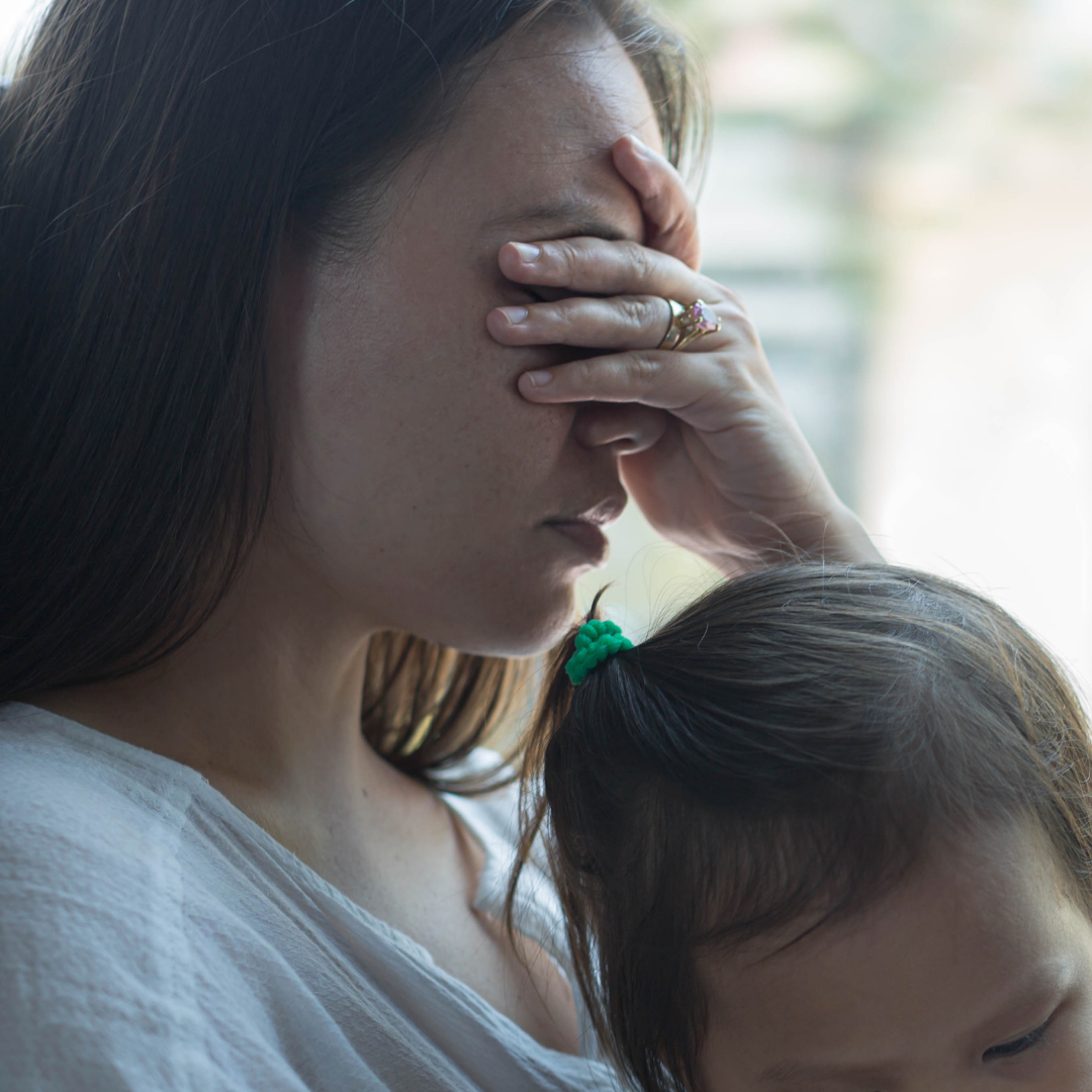 A worn-out mother holds her baby, hand over her eyes, caught in a moment of exhaustion and overwhelm. This is what it looks like when the nervous system is flooded — and it's one of the most overlooked factors in why sleep training doesn't work.