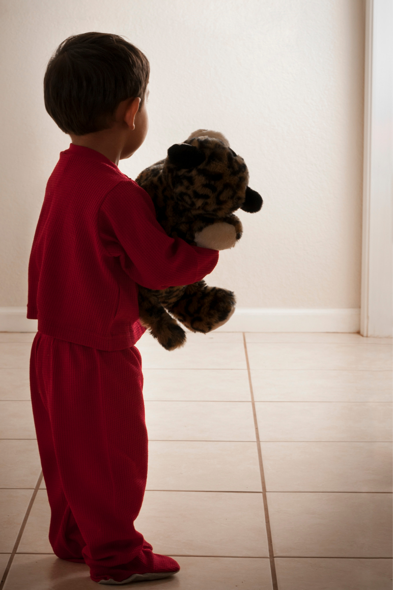 Toddler in the hallway in pajamas with his teddy bear, leaving his bedroom at bedtime because he can't sleep.