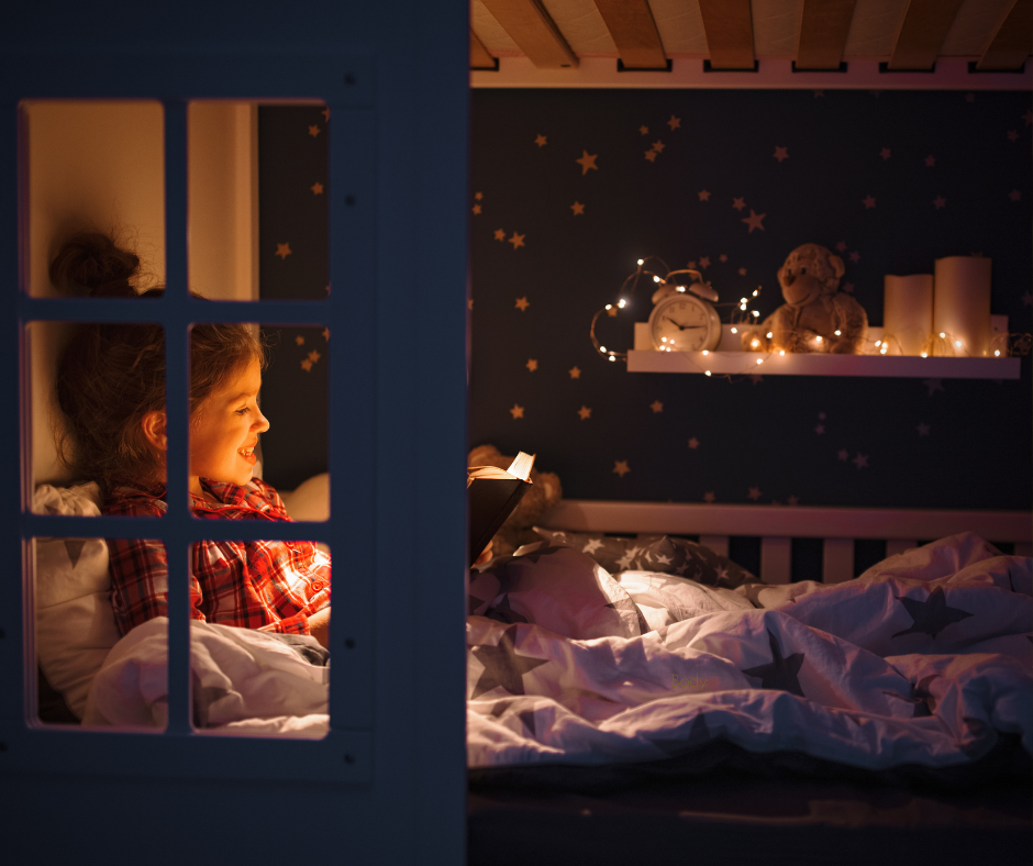 A young girl reads in a cozy, dark bedroom nook with soft string lights, illustrating the kind of calm, sensory-friendly sleep environment that helps neurodivergent children settle at night.