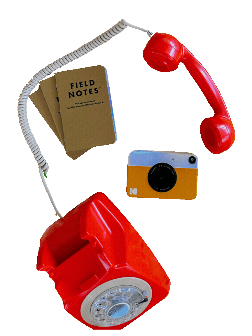 Red rotary phone, a small vintage camera, a notebook labeled 'Field Notes', and a white cord with a telephone receiver attached.