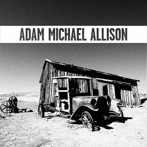 Black and white image of an abandoned old car and rustic wooden building in a desert landscape with clear sky. Text "Adam Michael Allison" at the top.