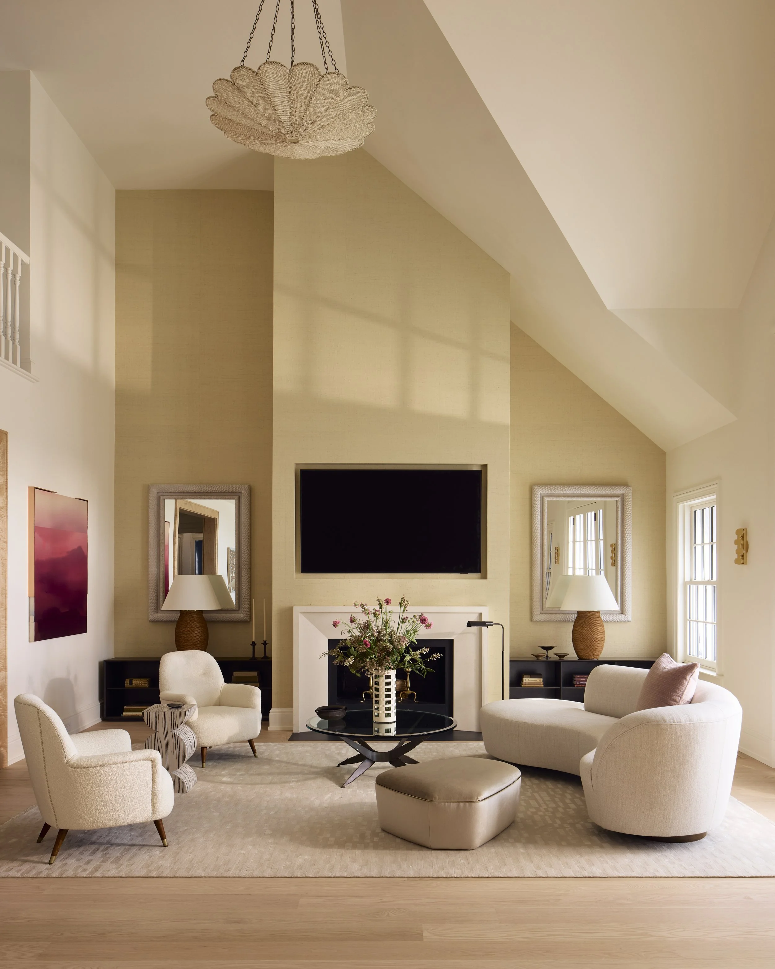 The double height living room features an original wood burning fireplace. The seating area elegantly balances vintage and modern furniture, anchored by a custom wool and silk rug whose design was inspired by light reflecting off water ripples.