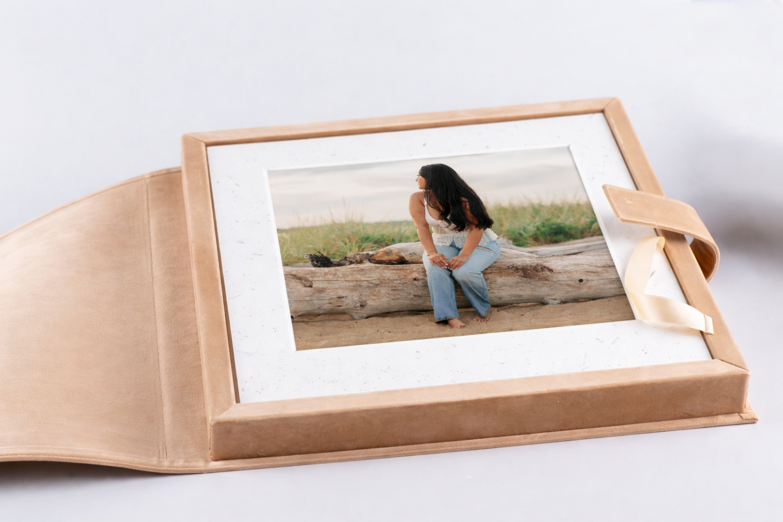 A woman sitting on a log on the beach, viewed through a framed photograph in a beige photo album.