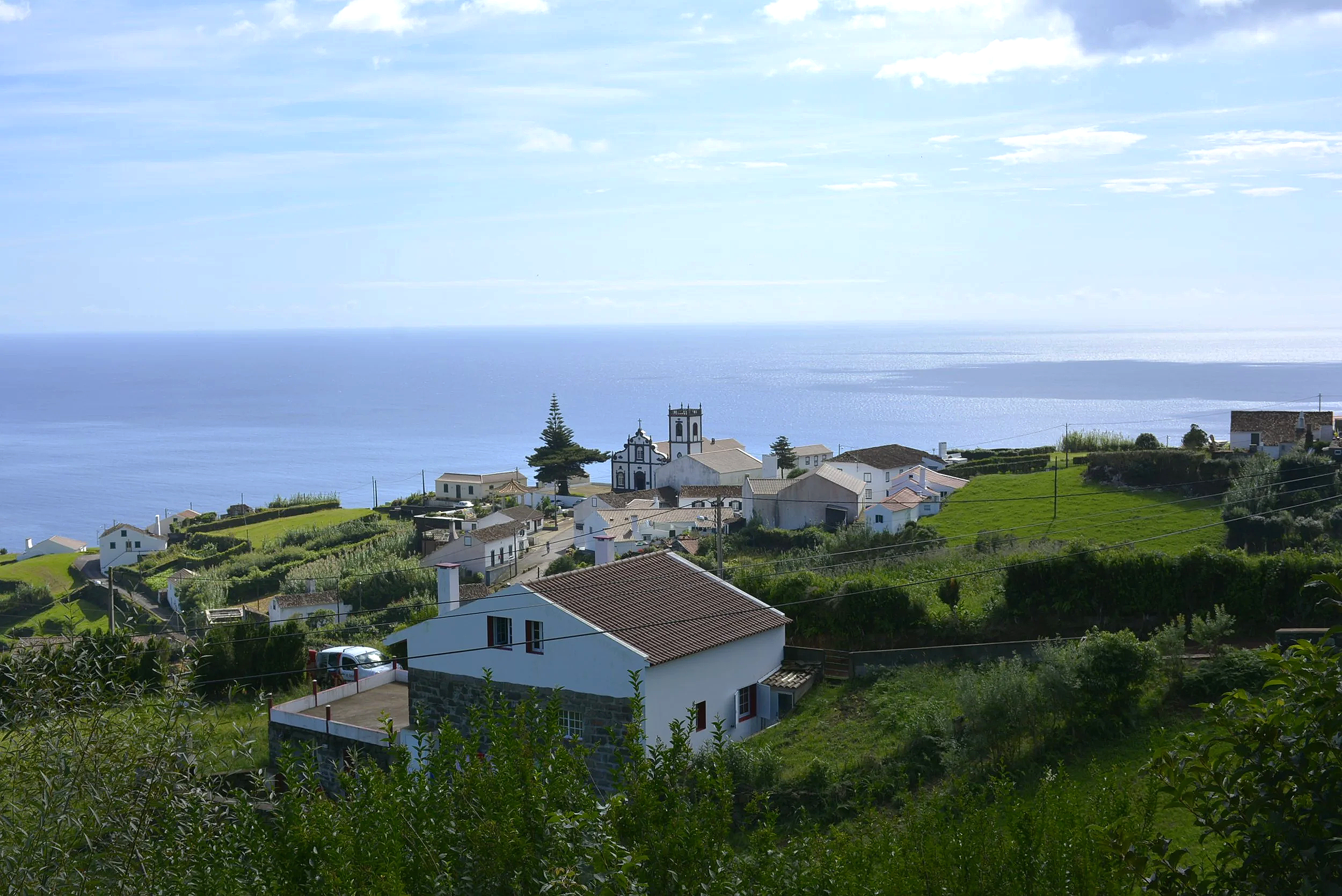 Scenic view of a coastal village with white houses, churches, and lush greenery overlooking the ocean.