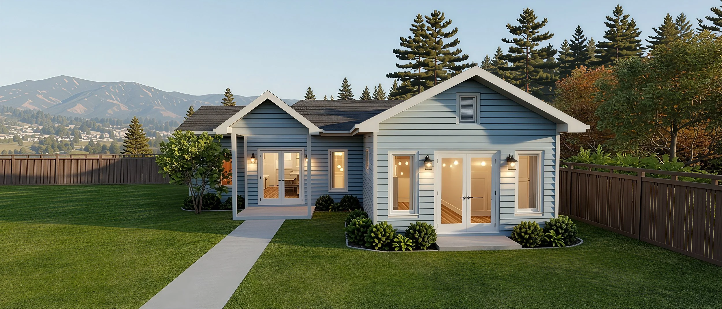 A modern blue house with a yard, surrounded by a wooden fence, with mountains and trees in the background, and interior lights visible through the windows and doors.