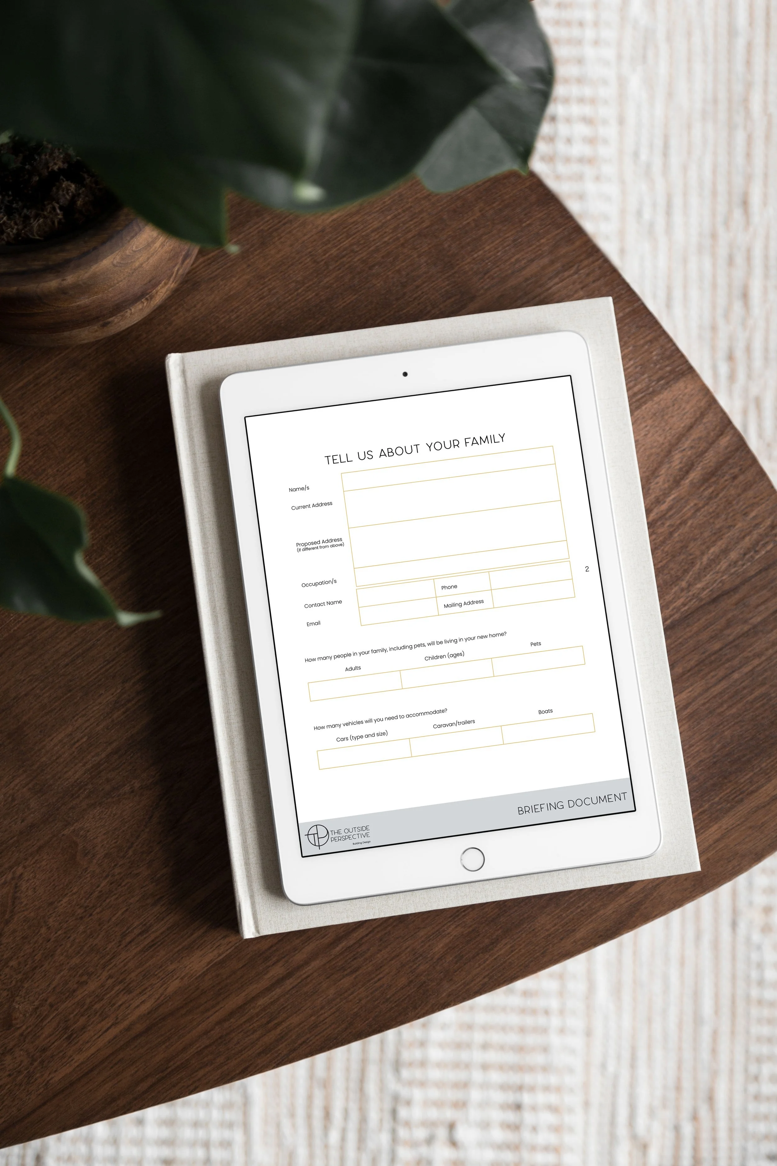 Tablet on a book, displaying a briefing information form, placed on a wooden table next to a plant.