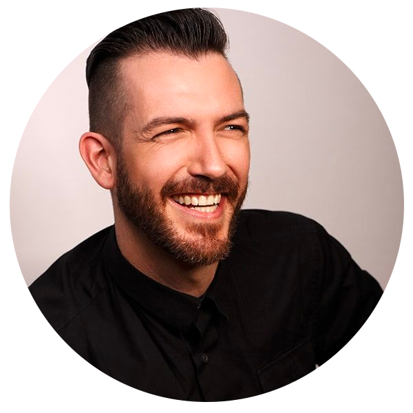 A smiling man with a beard and short dark hair, wearing a black shirt, against a neutral background.