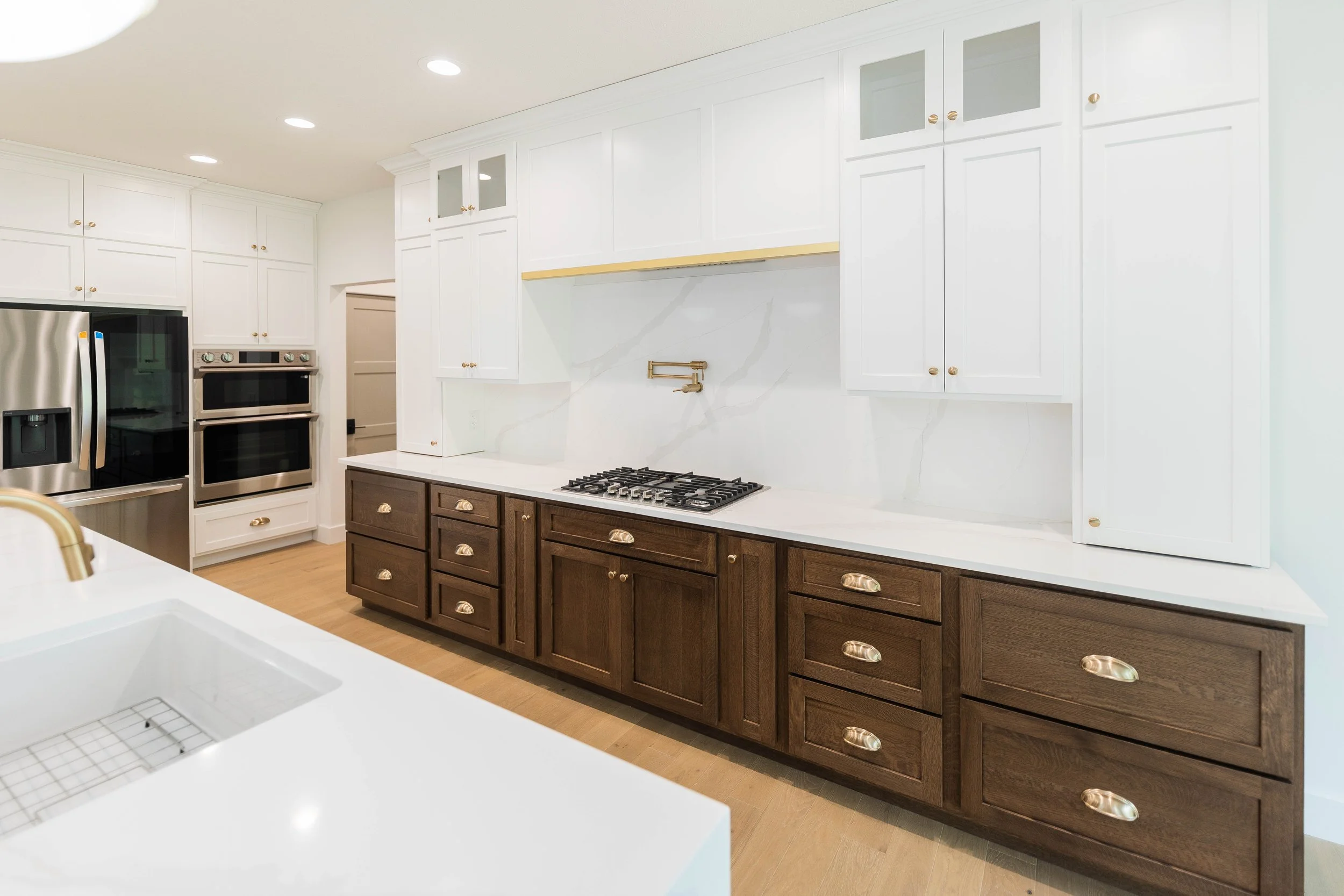Modern kitchen with white upper cabinets, dark wood lower cabinets, marble backsplash, built-in double oven, and stainless steel refrigerator.