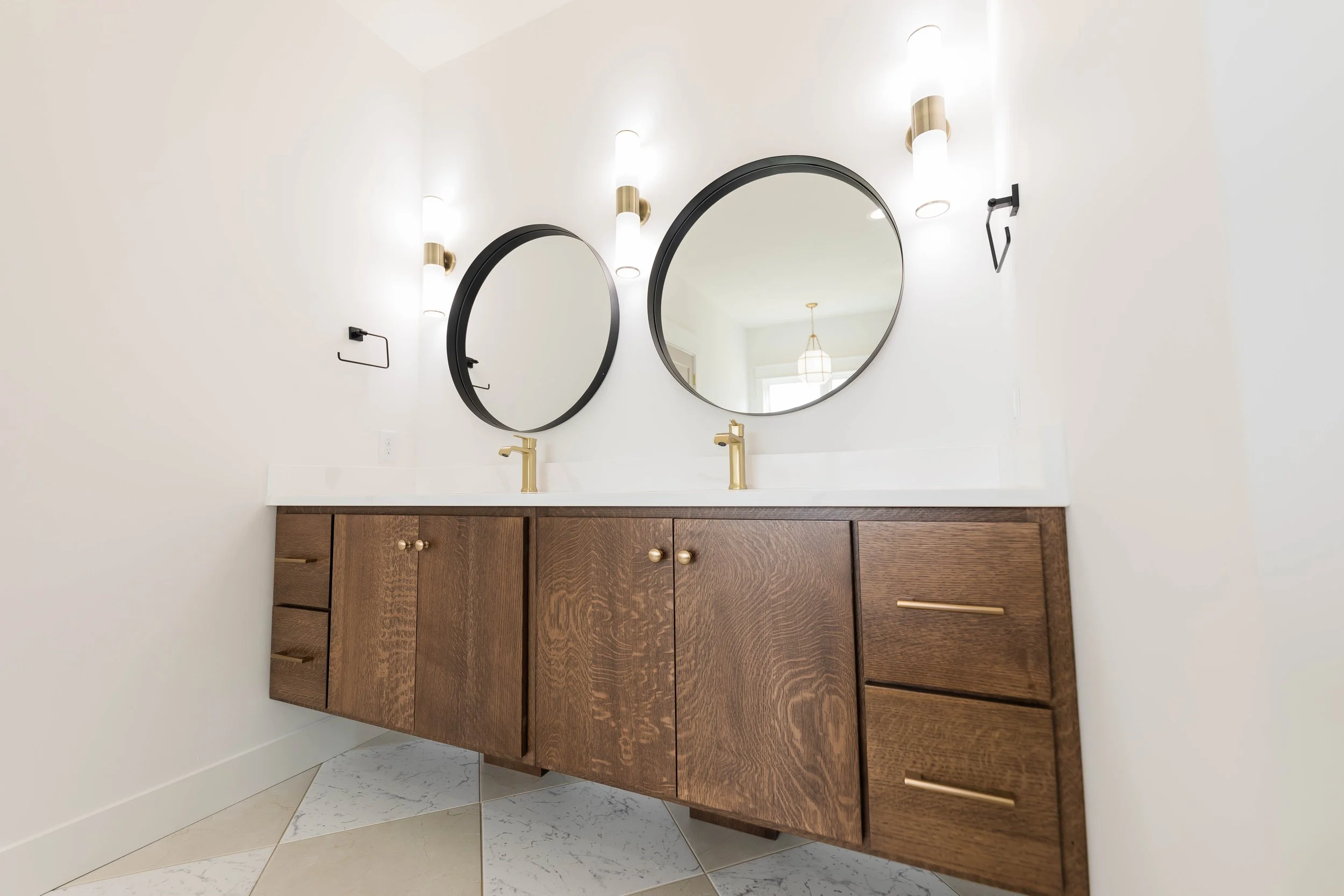 A bathroom vanity with two round mirrors, gold faucets, and wall-mounted lights.