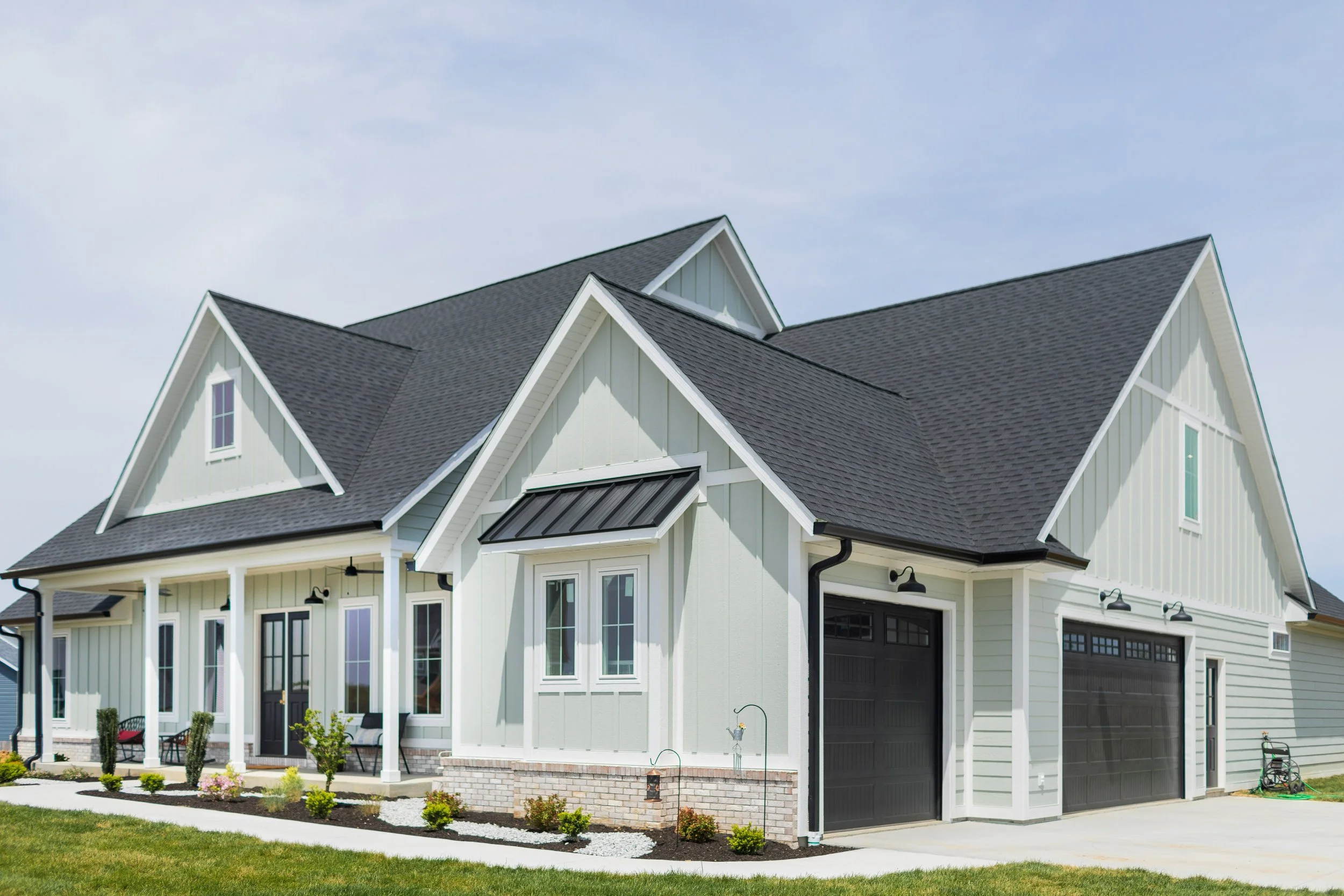 Modern two-story house with white siding, black garage doors, gabled roof, and front porch with seating
