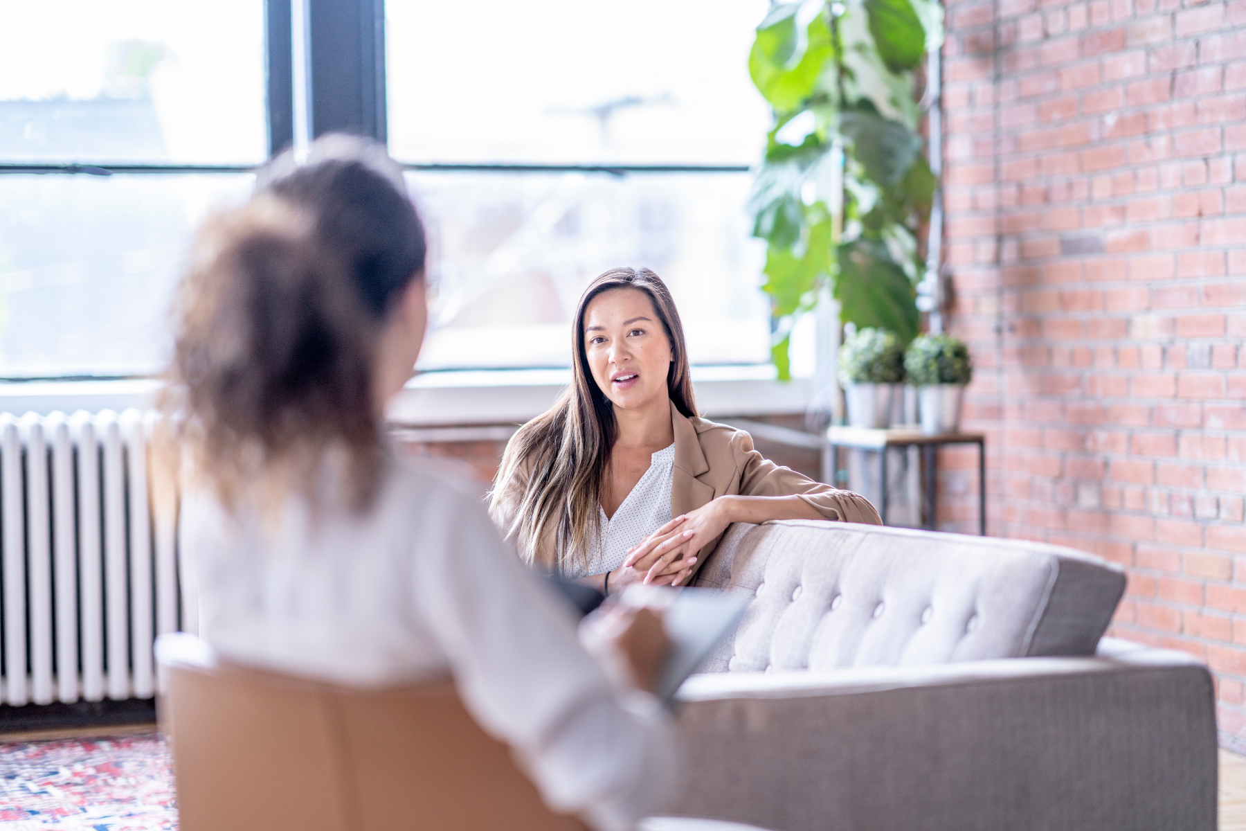 A therapist chats with a patient, who's sitting on a gray couch.