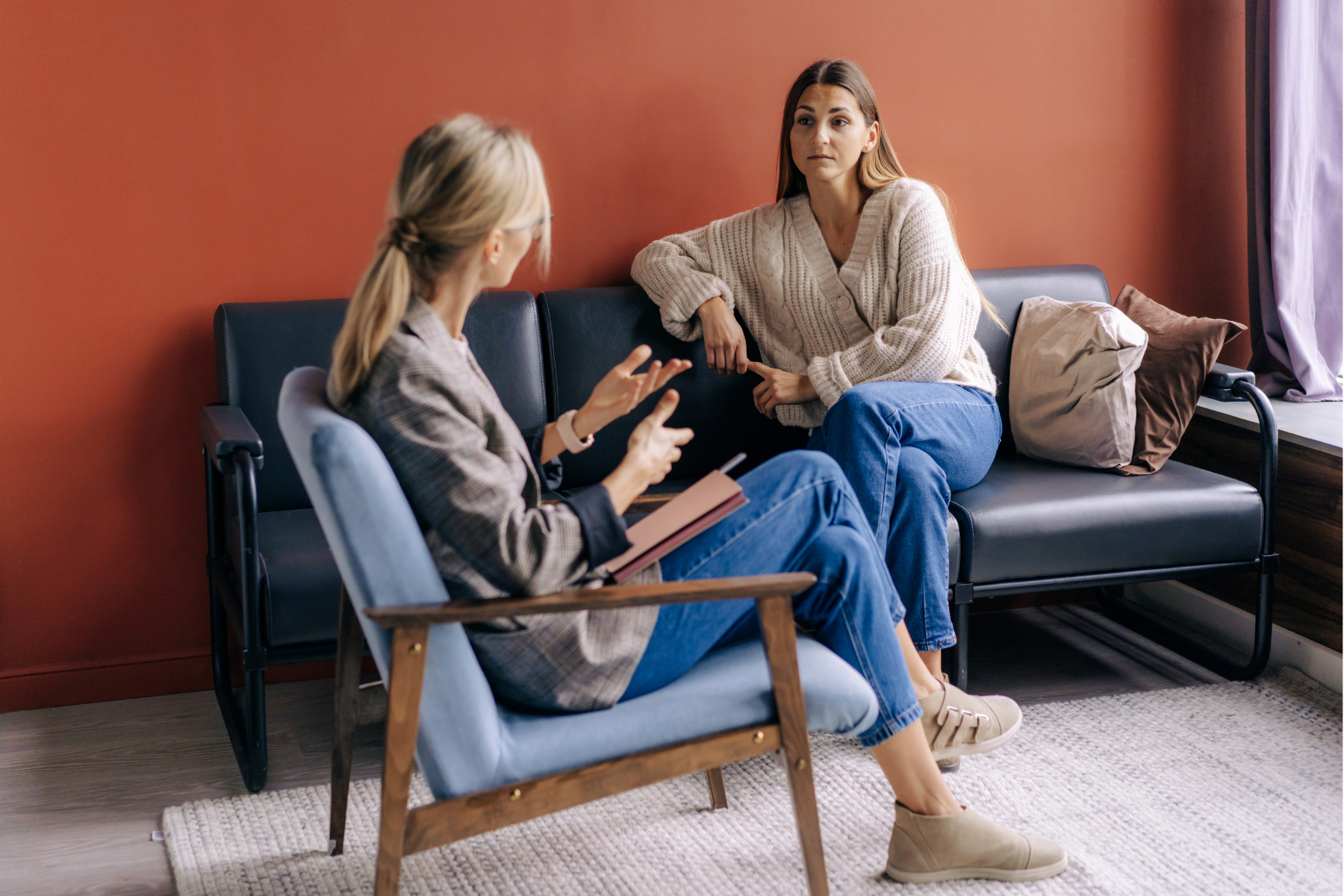 A woman sits on a dark couch, talking with her therapist