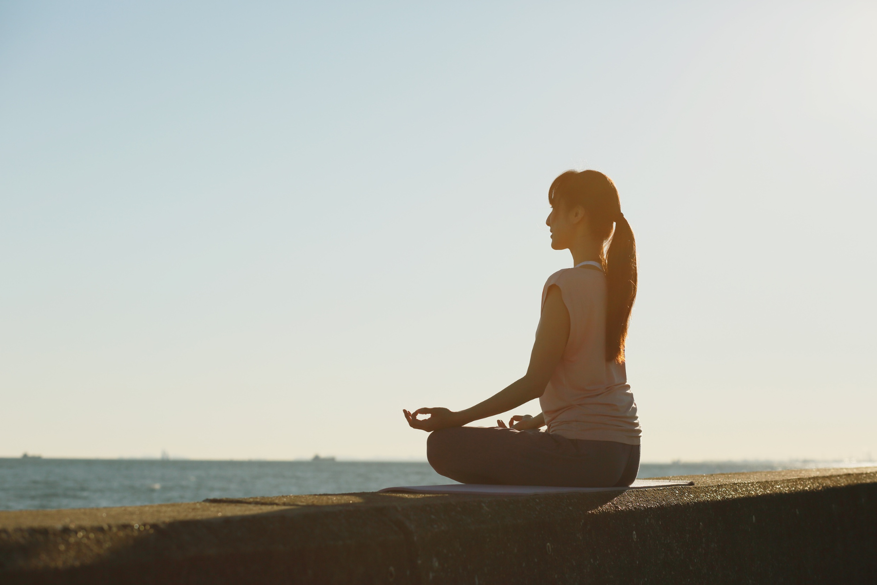 a woman sits cross-legged, looking out over the water