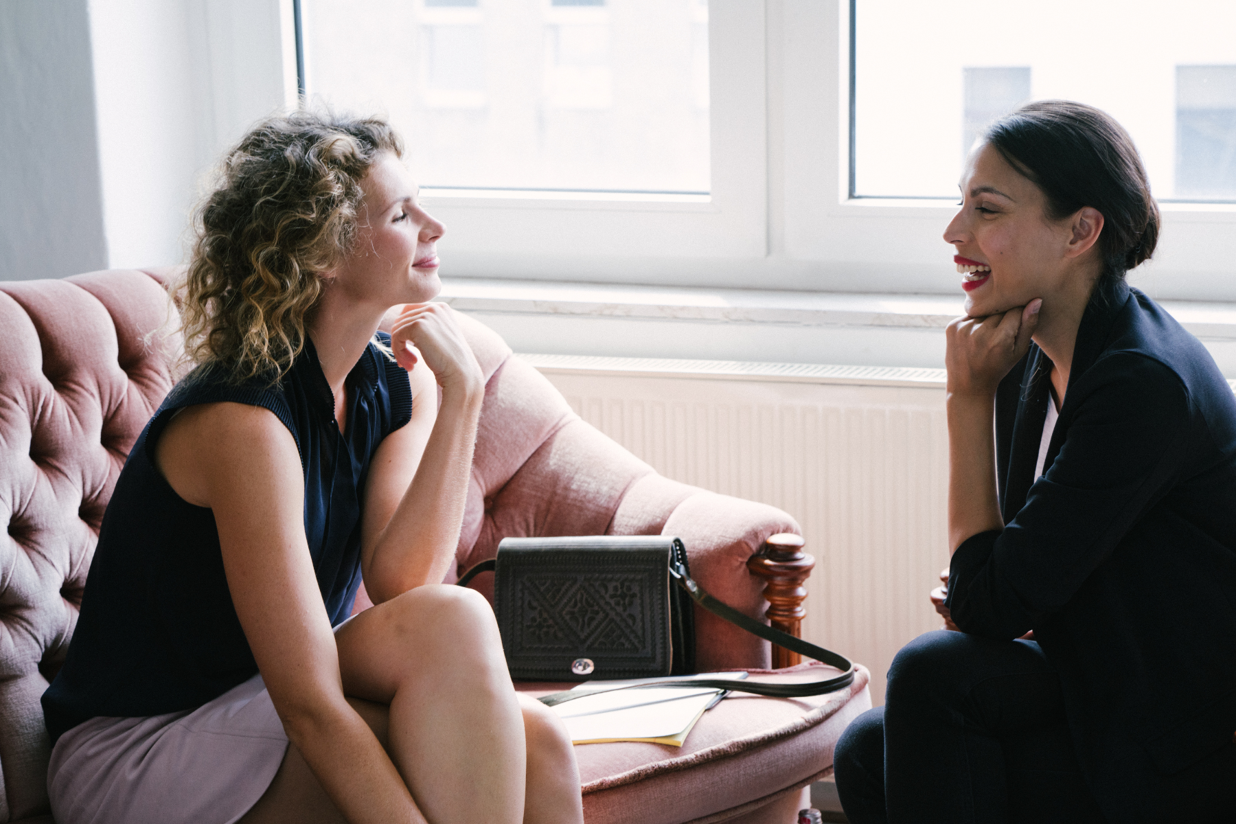 A woman sits on a pink couch, meeting with her therapist.