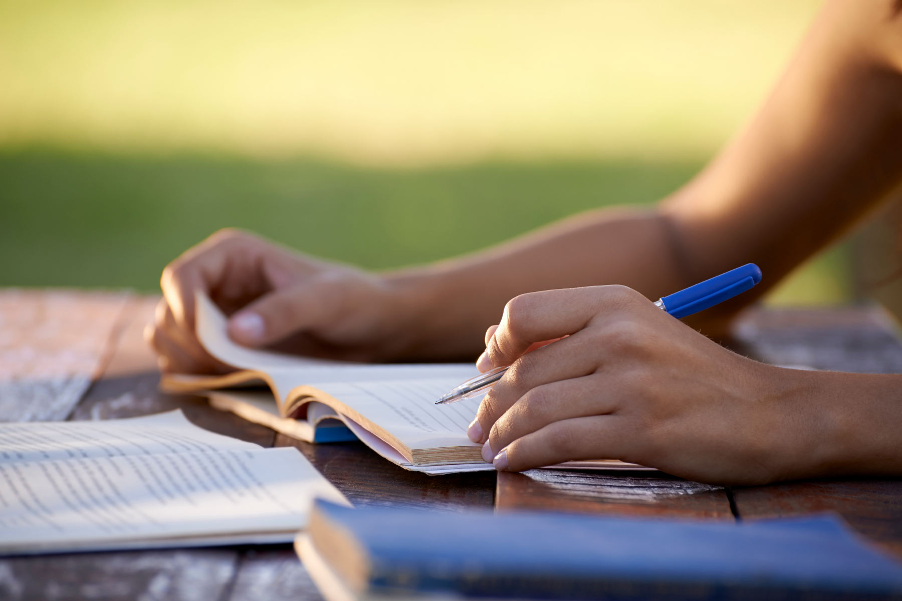A photograph of someone's hands writing in a notebook with a blue pen.