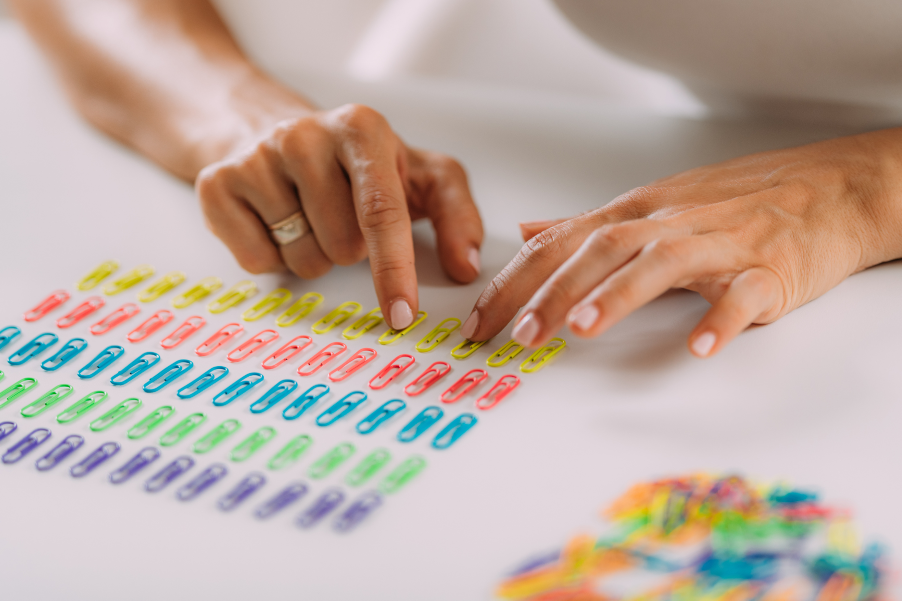 A woman lines up paper clips in rows by color.