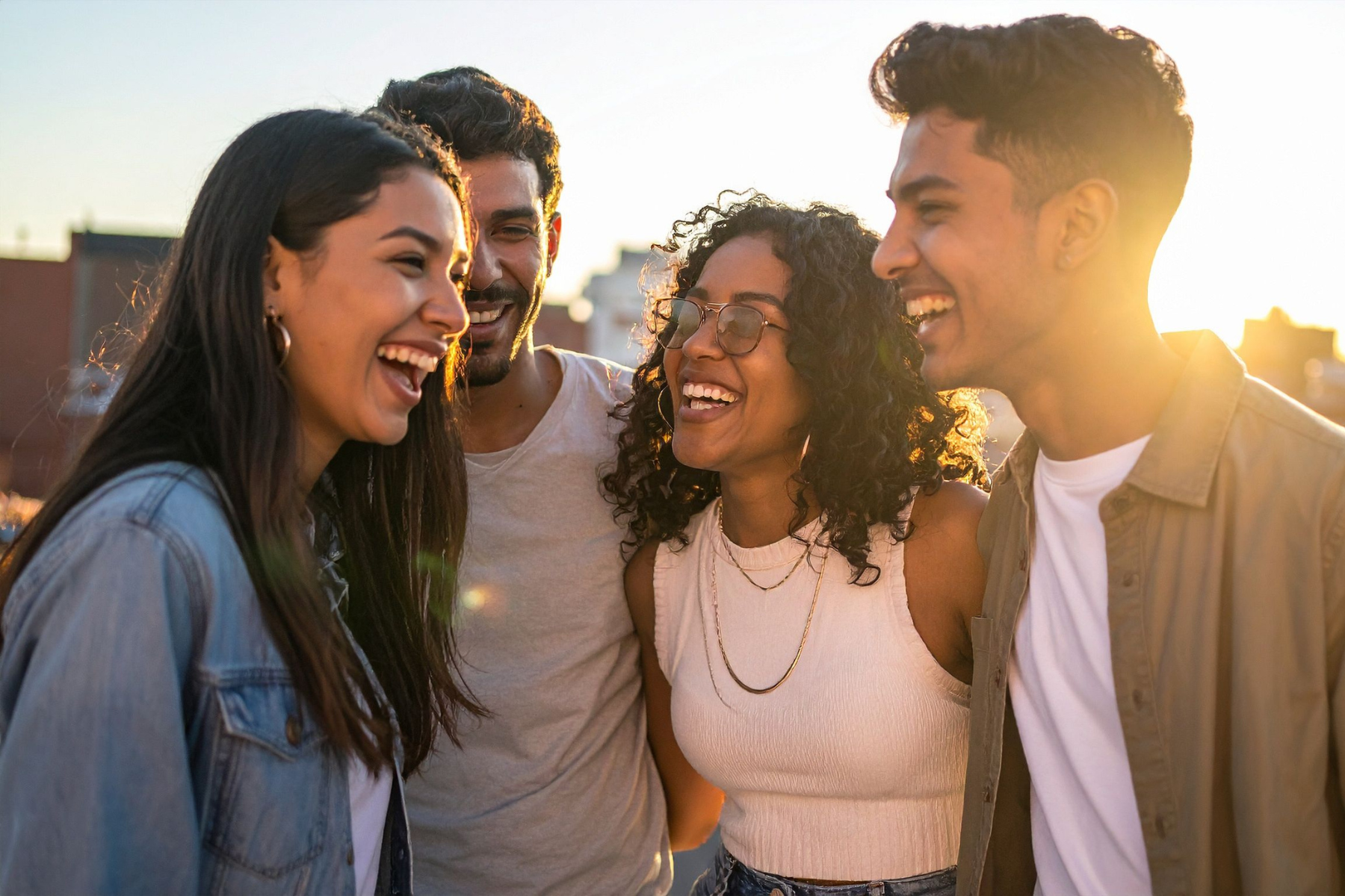 A group of four people stands close together at golden hour, smiling and laughing.