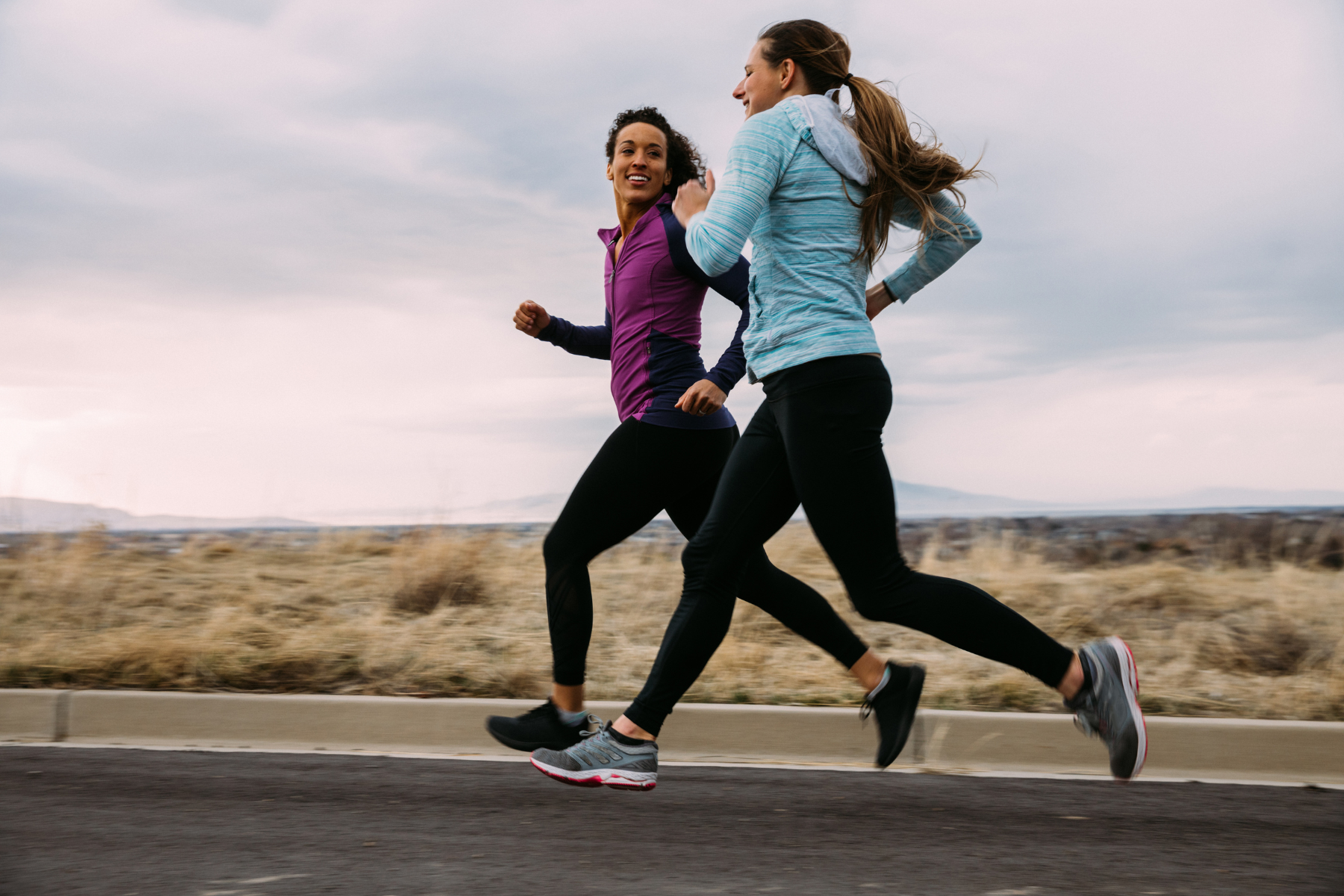 Two women go running together on the road, smiling