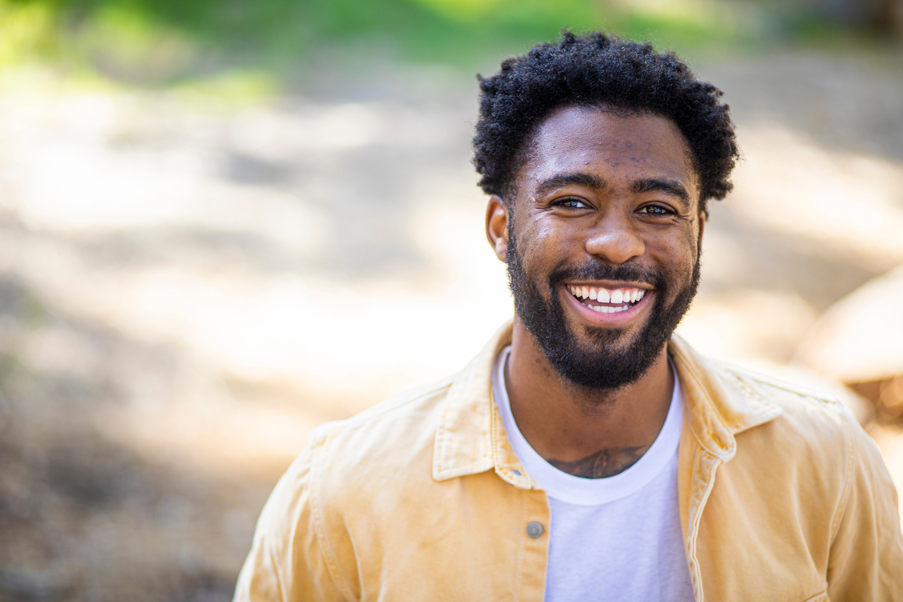 An African-American man looks into the camera, smiling. He's wearing a yellow button-up with a white shirt underneath.