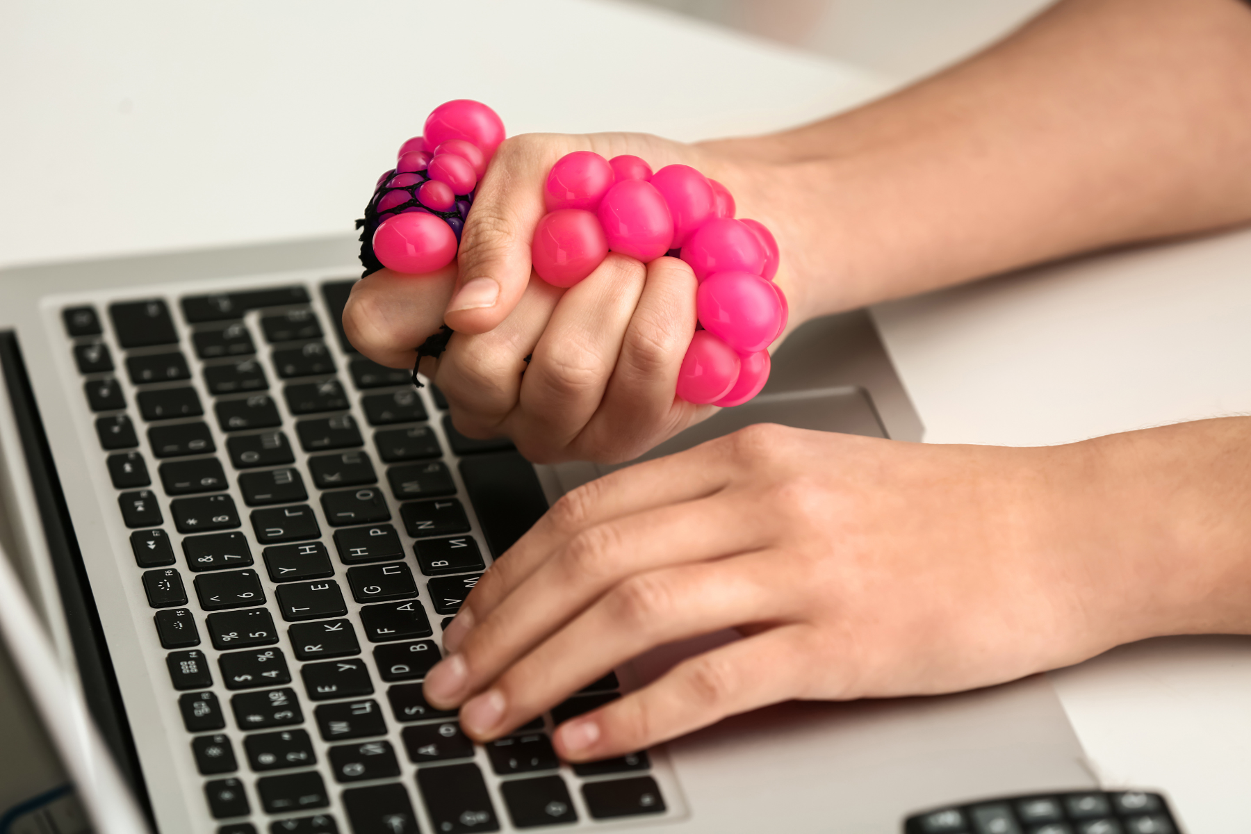 A person clutches a pink sensory tool while typing on a laptop.