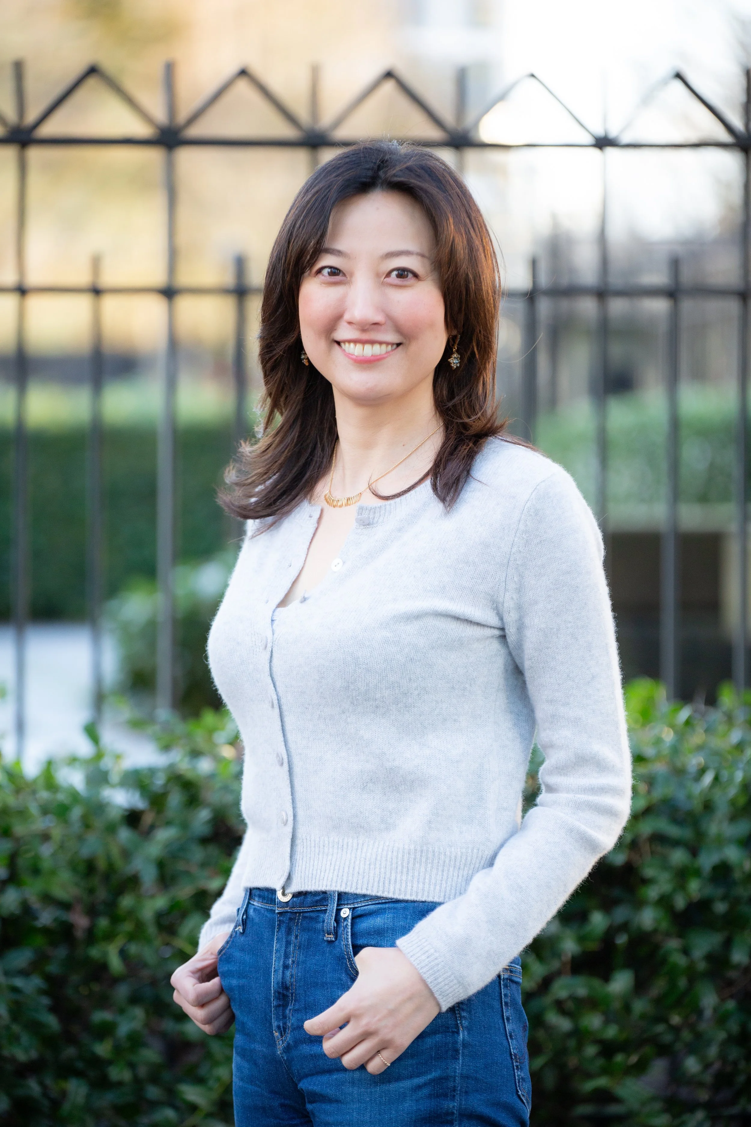 Ryoka Kim stands in front of a gate. She is wearing a gray sweater, has dark hair, and is smiling.