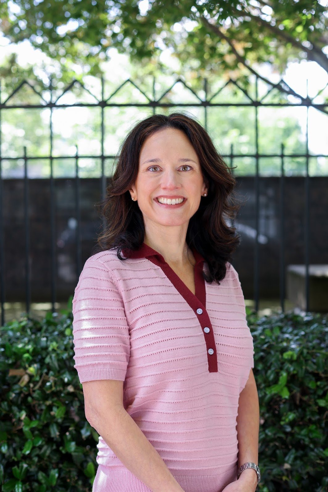 Jennie Jergerian, a therapist at Aspire Psychology, stands outside. She is smiling, has dark hair, and wears a pink shirt.