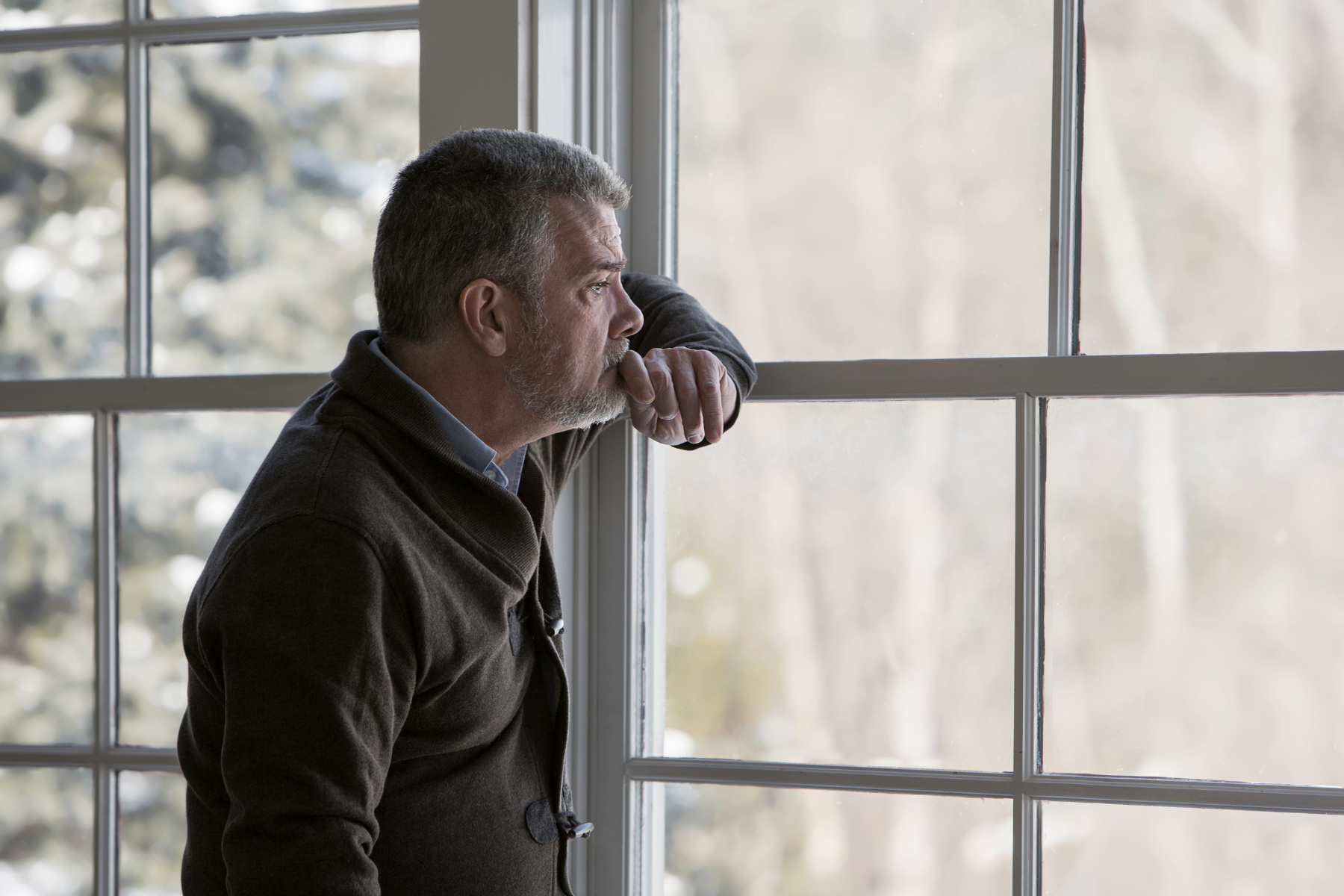 A man stares out a window, looking distressed
