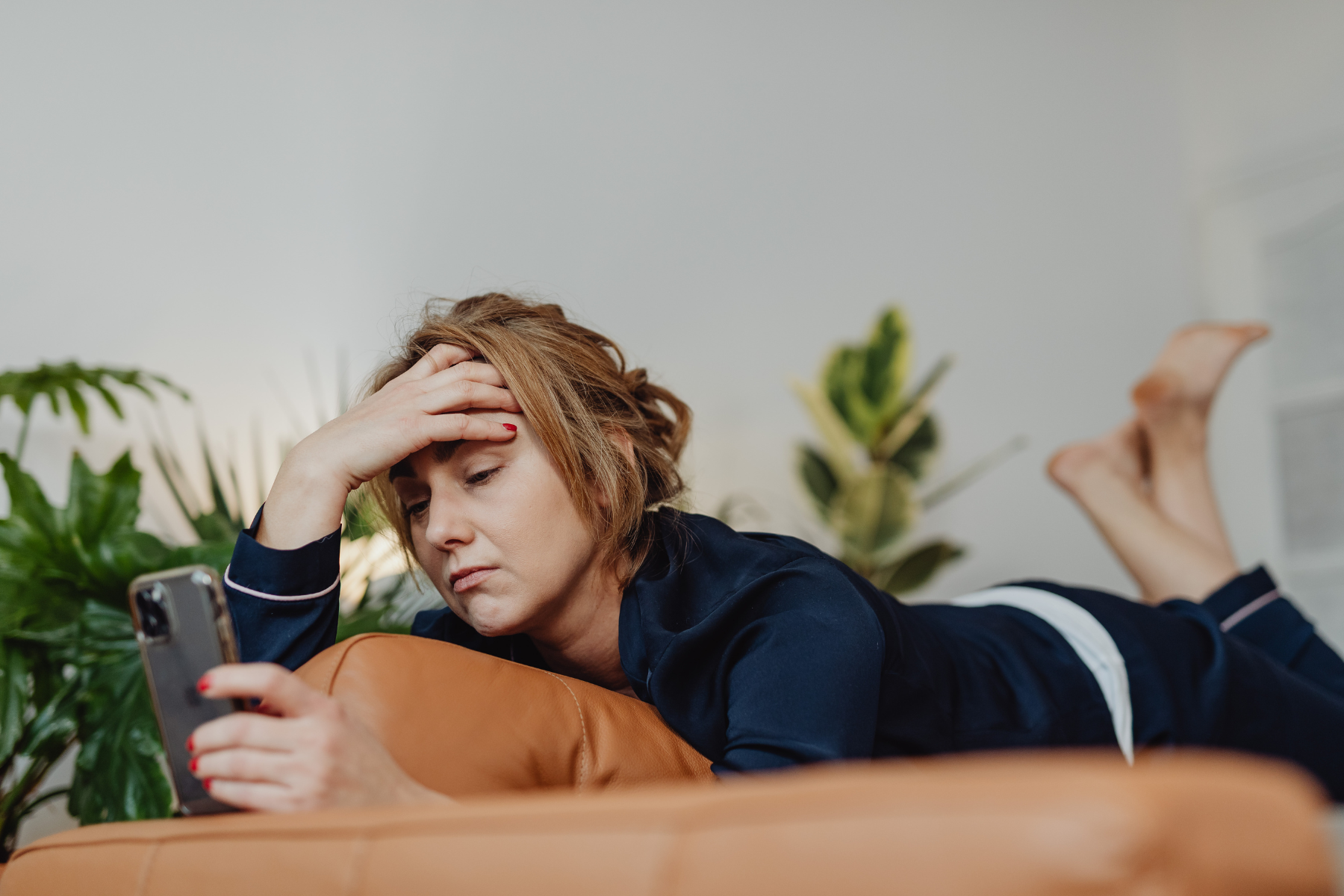 A tired-looking woman lays on her stomach, frowning at her phone.