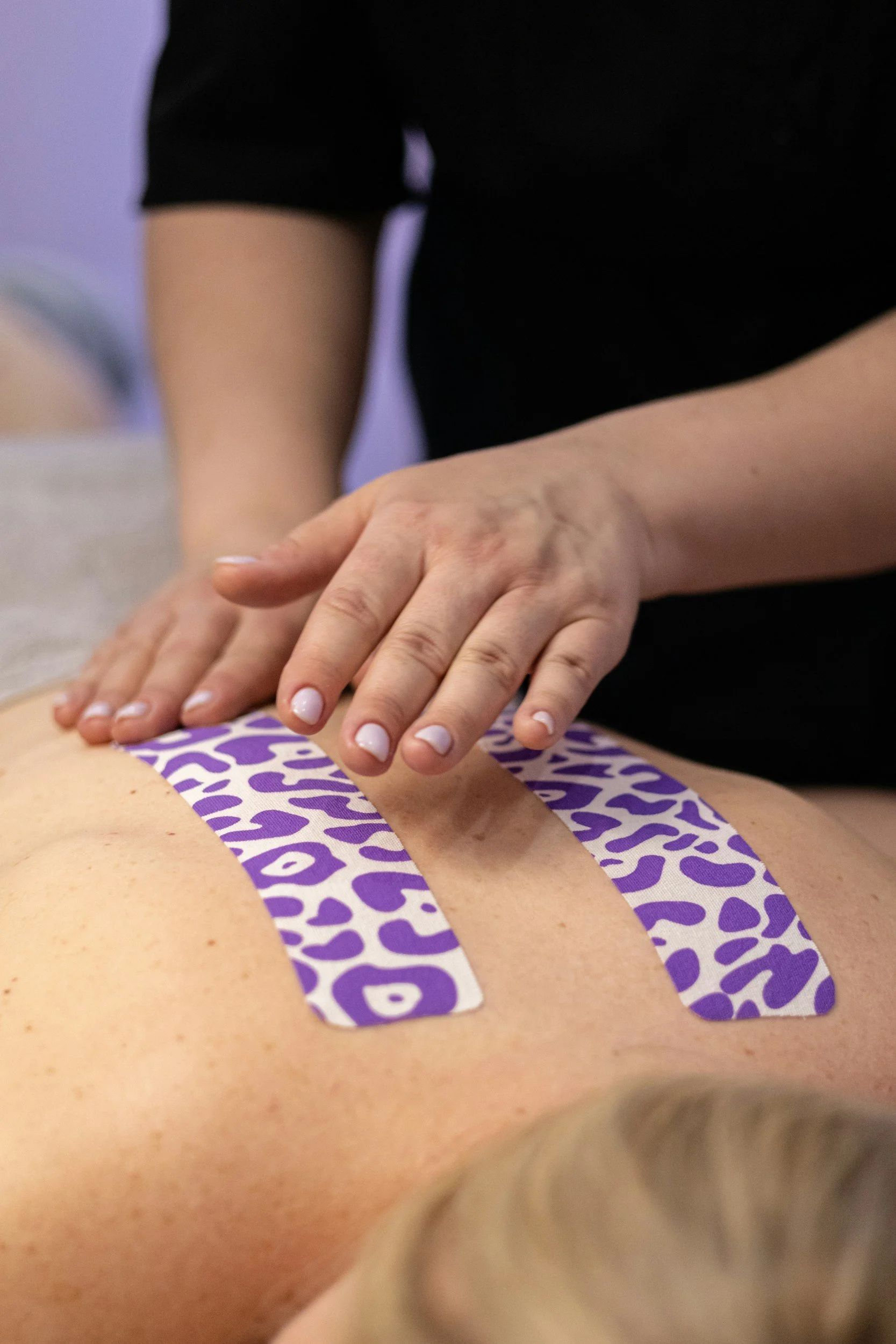 Practitioner performing abdominal massage on a person lying on a therapy table, with a logo saying 'Kind Body Wellness'.