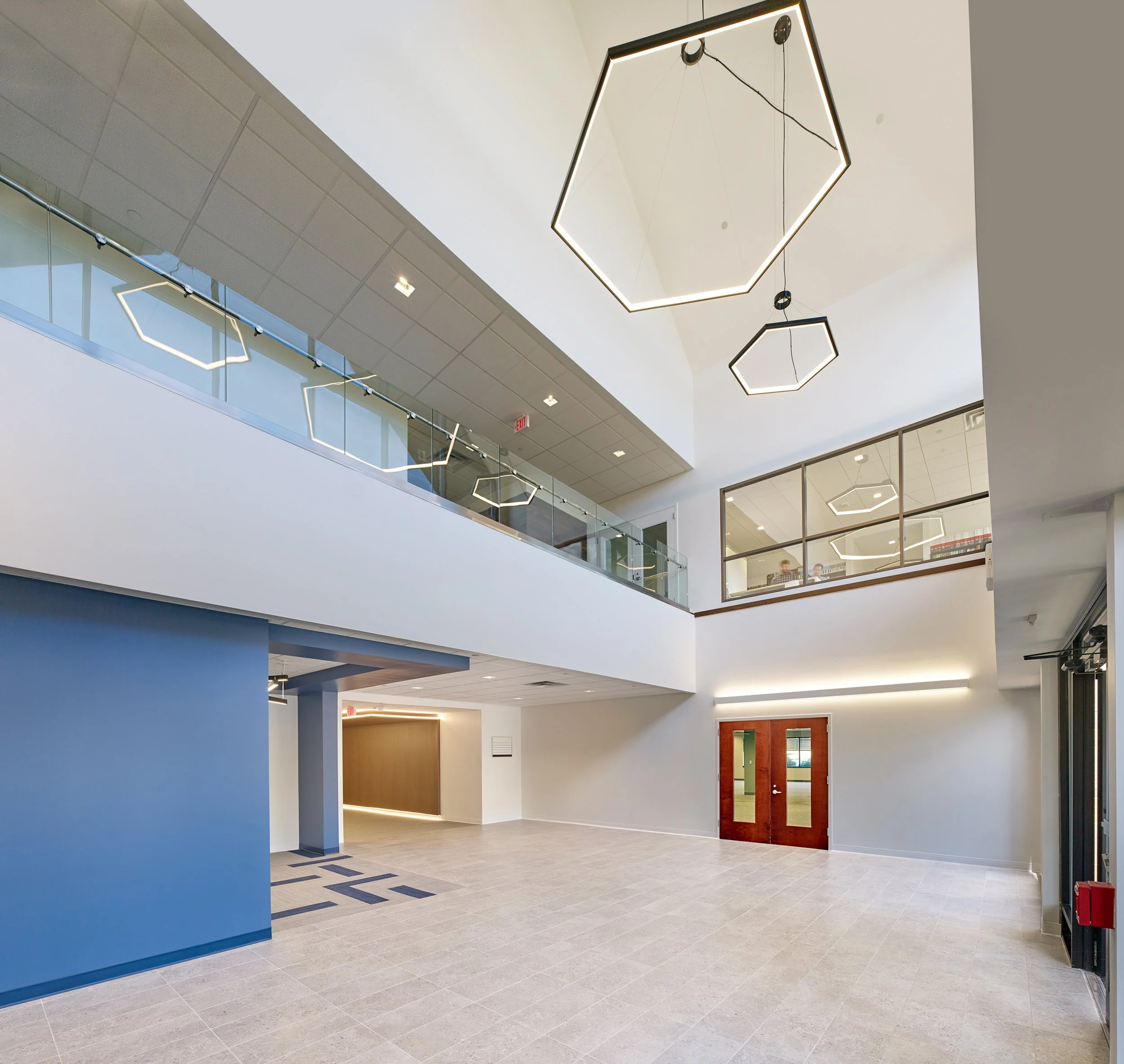 Modern indoor office space with gray tiled floor, white and light blue walls, and decorative hexagon-shaped ceiling lights.