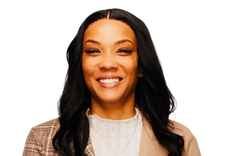 Smiling woman with long black hair, wearing a beige blazer and white top, against a white background.