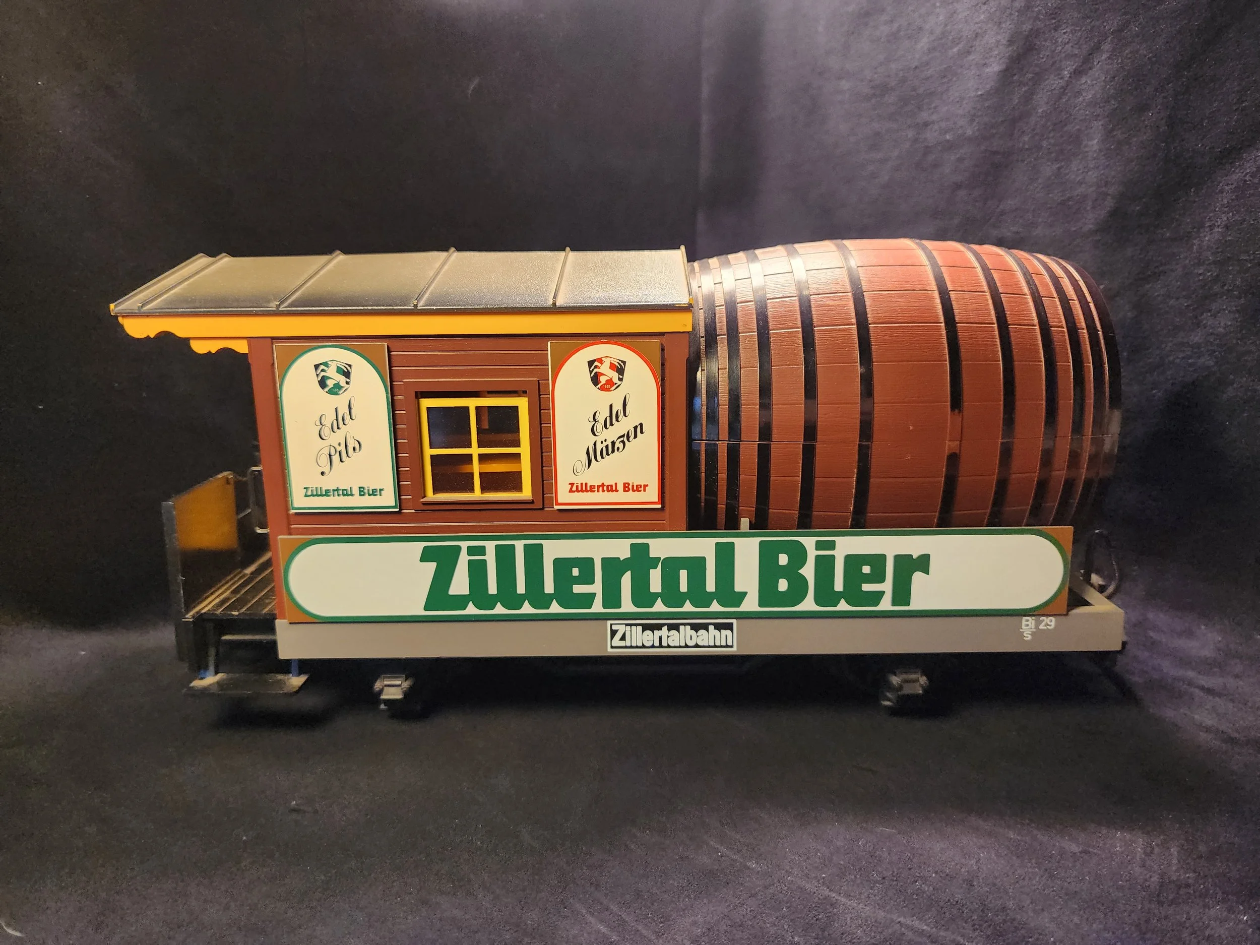 Model of a small building or train station with signs for Zillertal Bier, featuring a chimney and a curved roof, displayed on a black surface.
