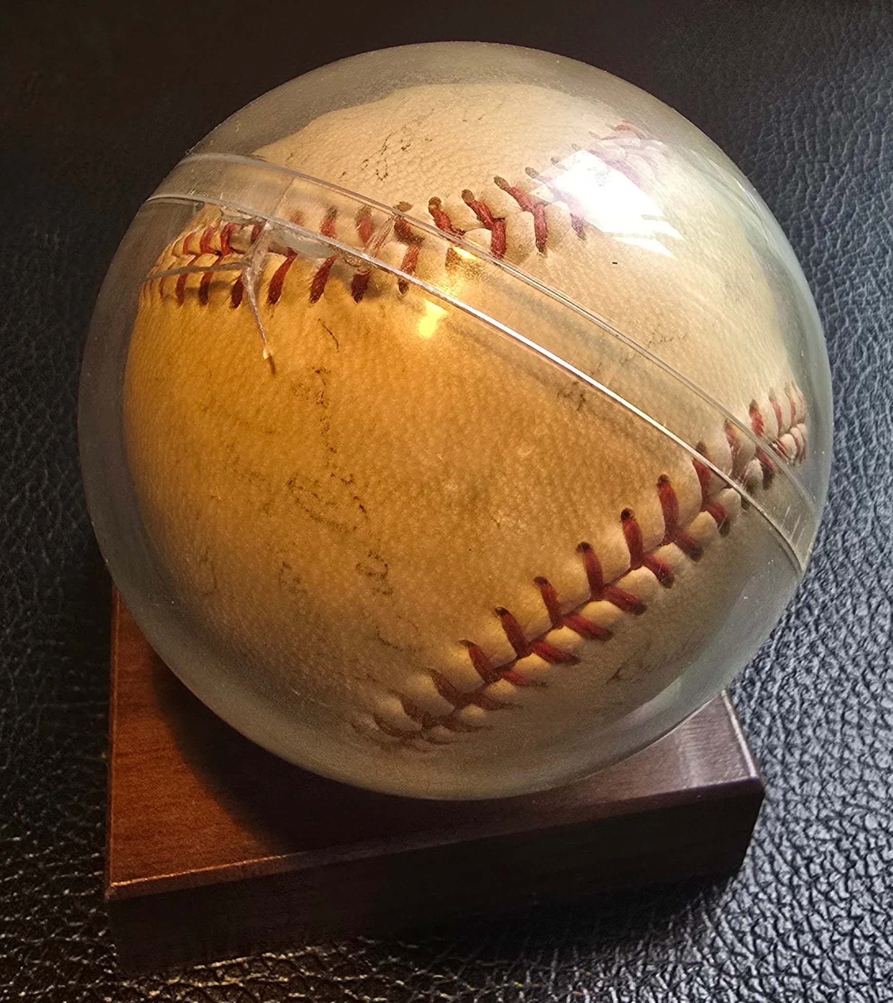 Close-up of a worn baseball with visible stitching, placed on a black textured surface.