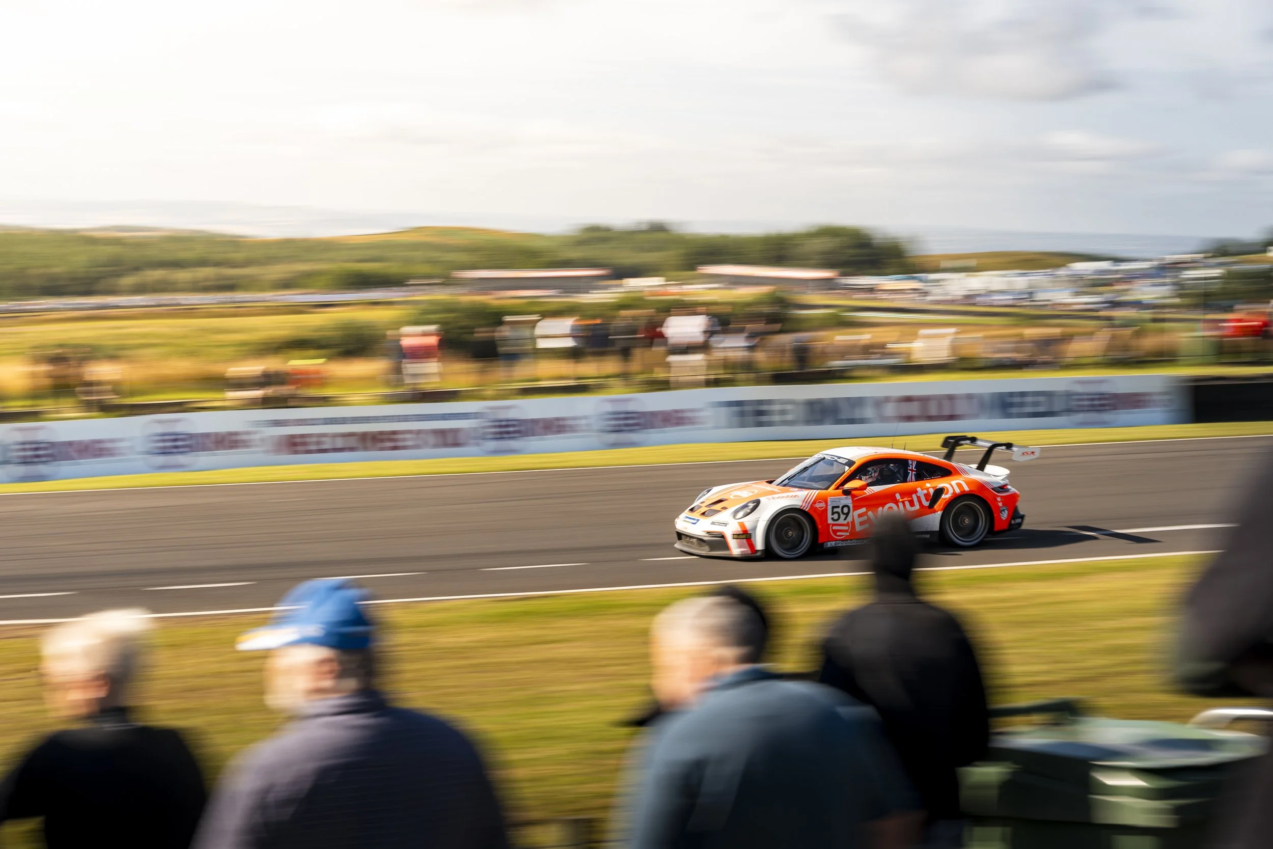 Race car speeding on track with blurred spectators in background and foreground. Knockhill Porsche Carrera Cup.