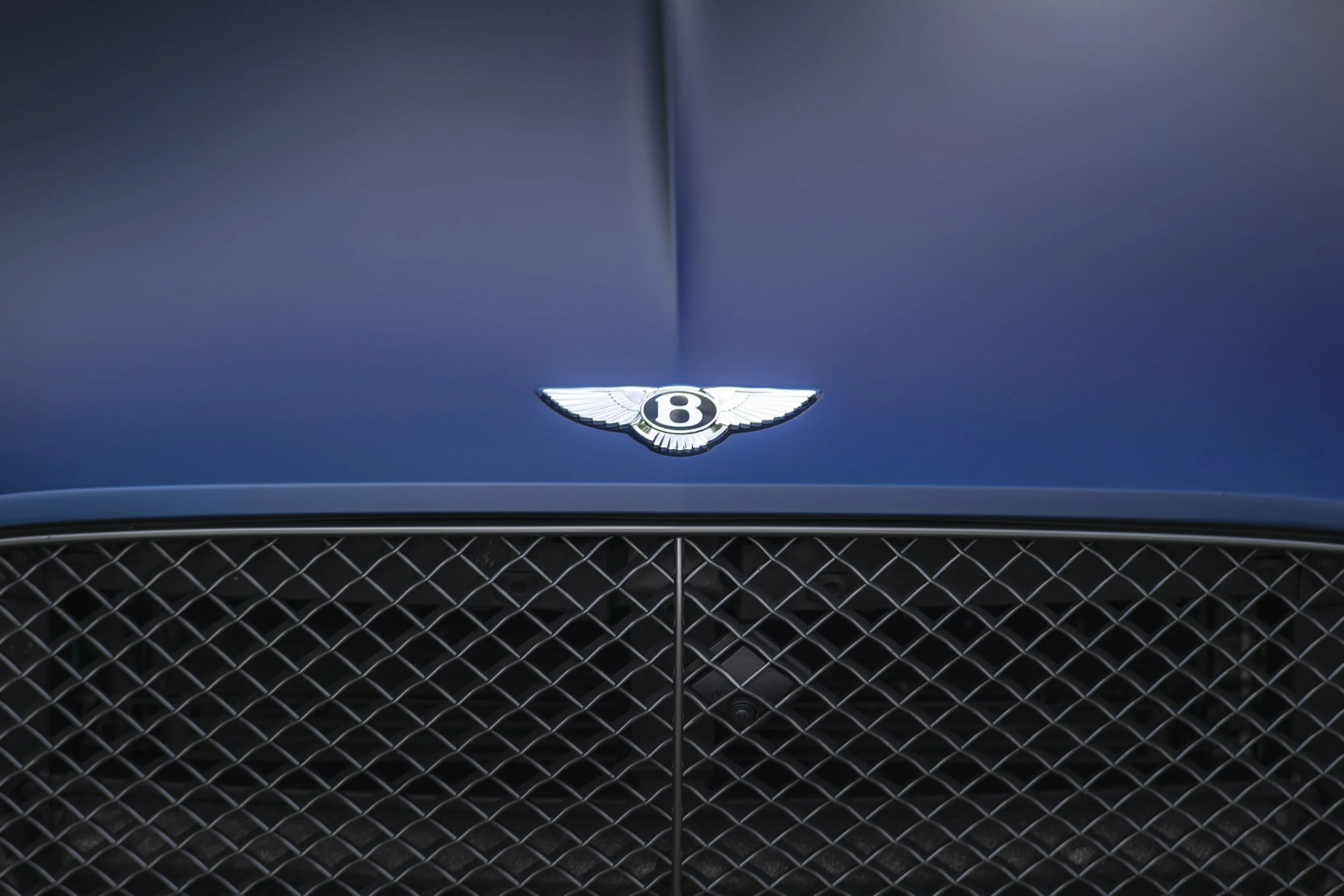 Close-up of a blue Bentley car's front grille with a Bentley emblem in the center.