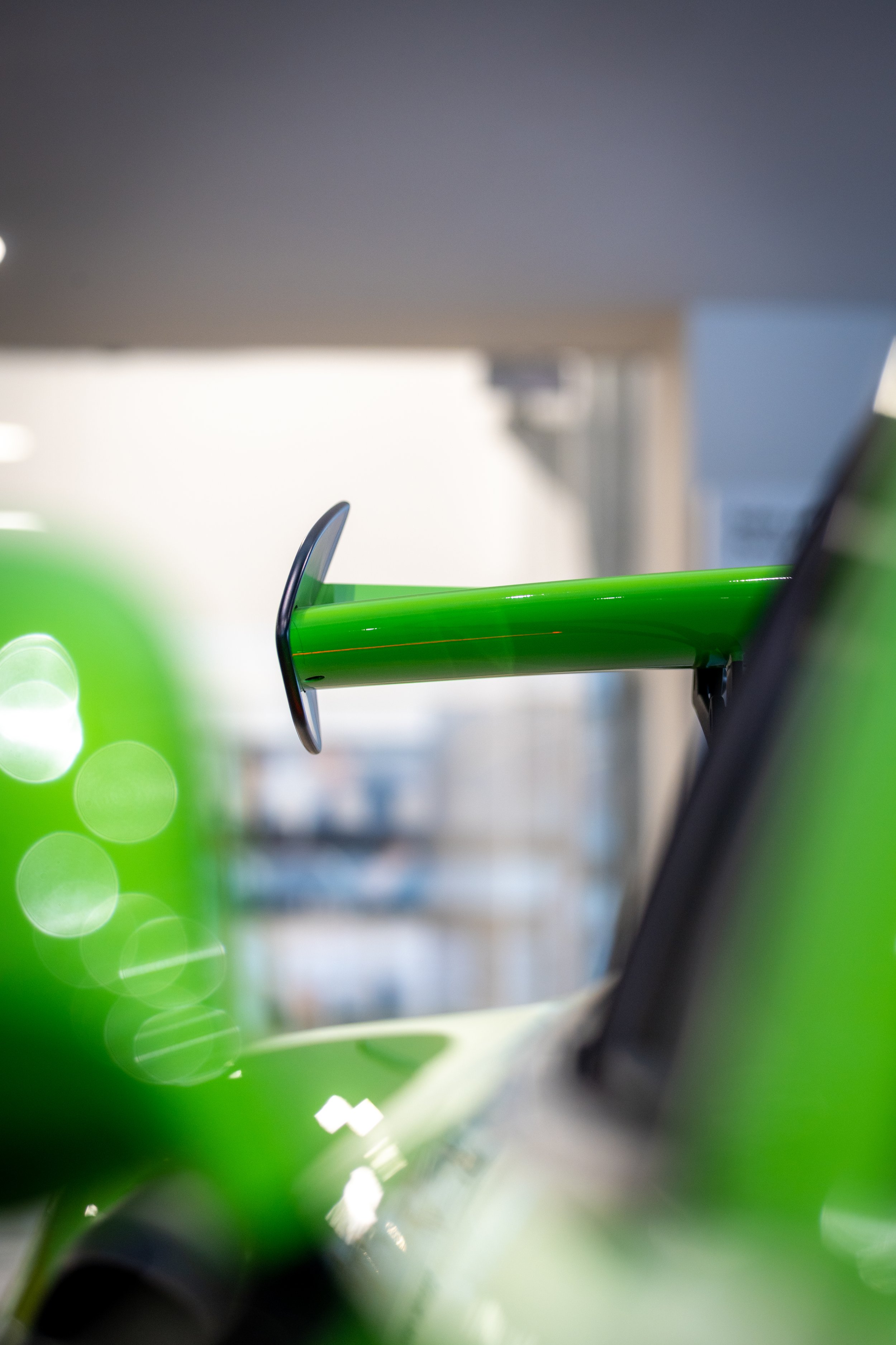 Close-up of a green drone with a black camera mounted underneath, set against a blurred background.