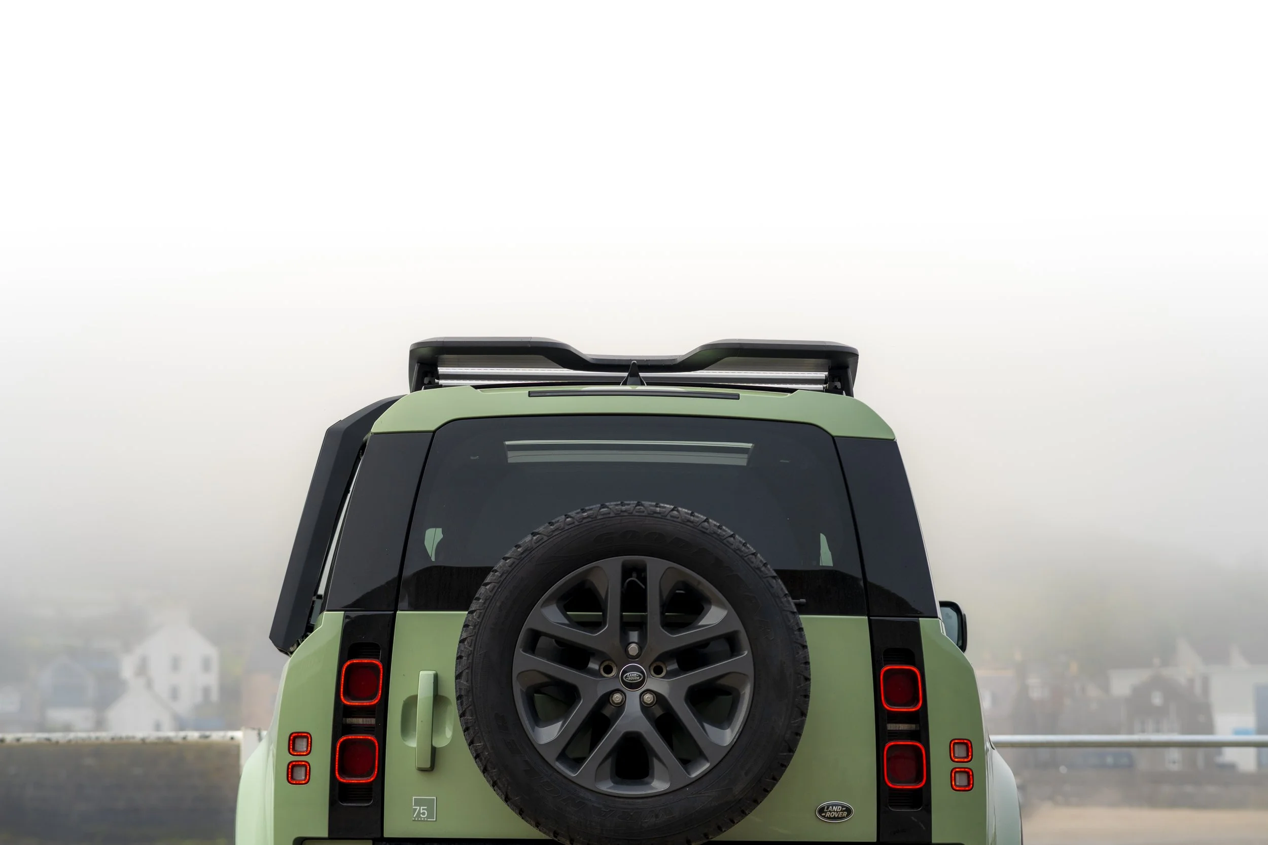 Green Land Rover Defender with spare tire on back, parked outdoors on an overcast day.