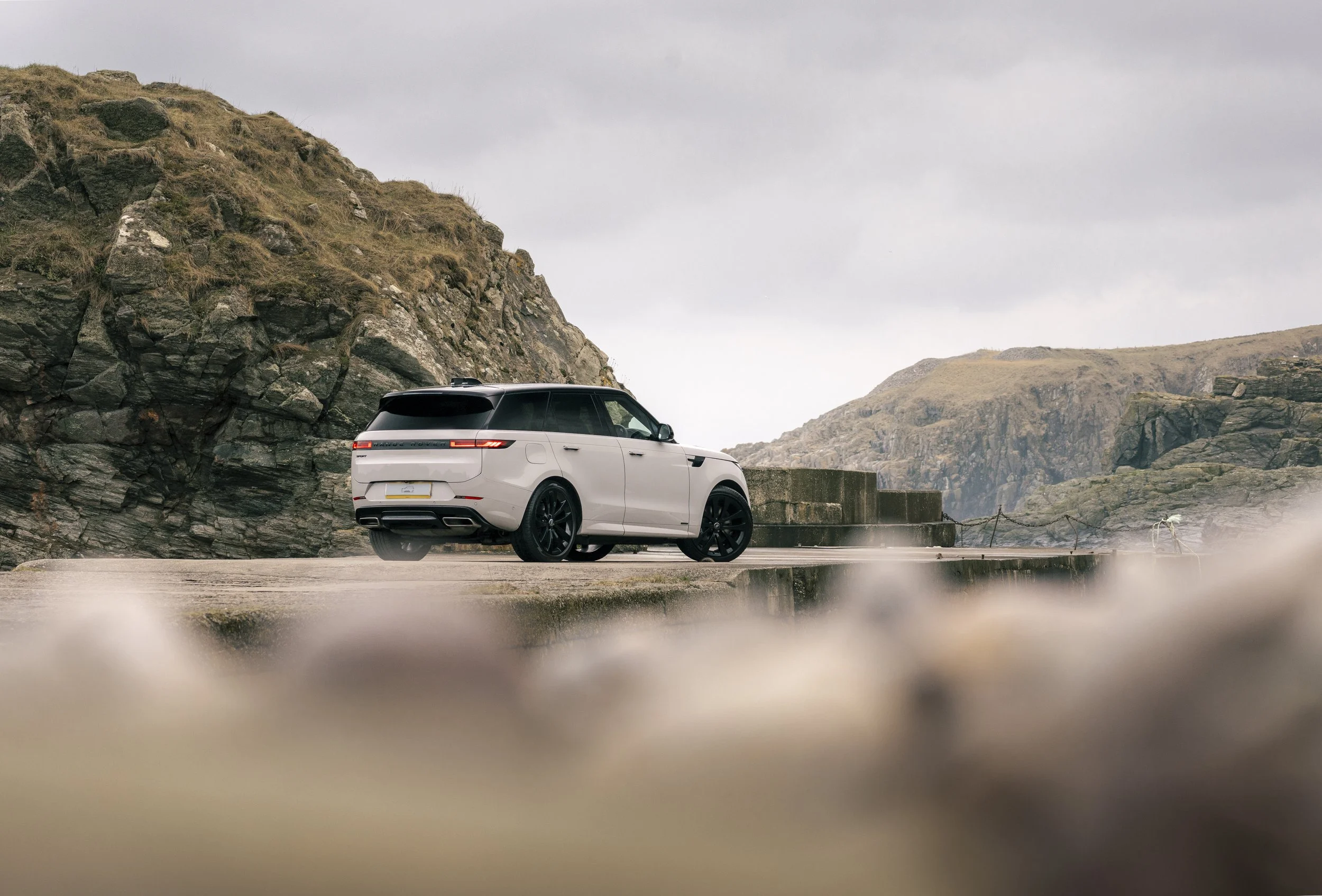 A silver SUV with black wheels parked on a concrete platform near rocky cliffs under a cloudy sky.