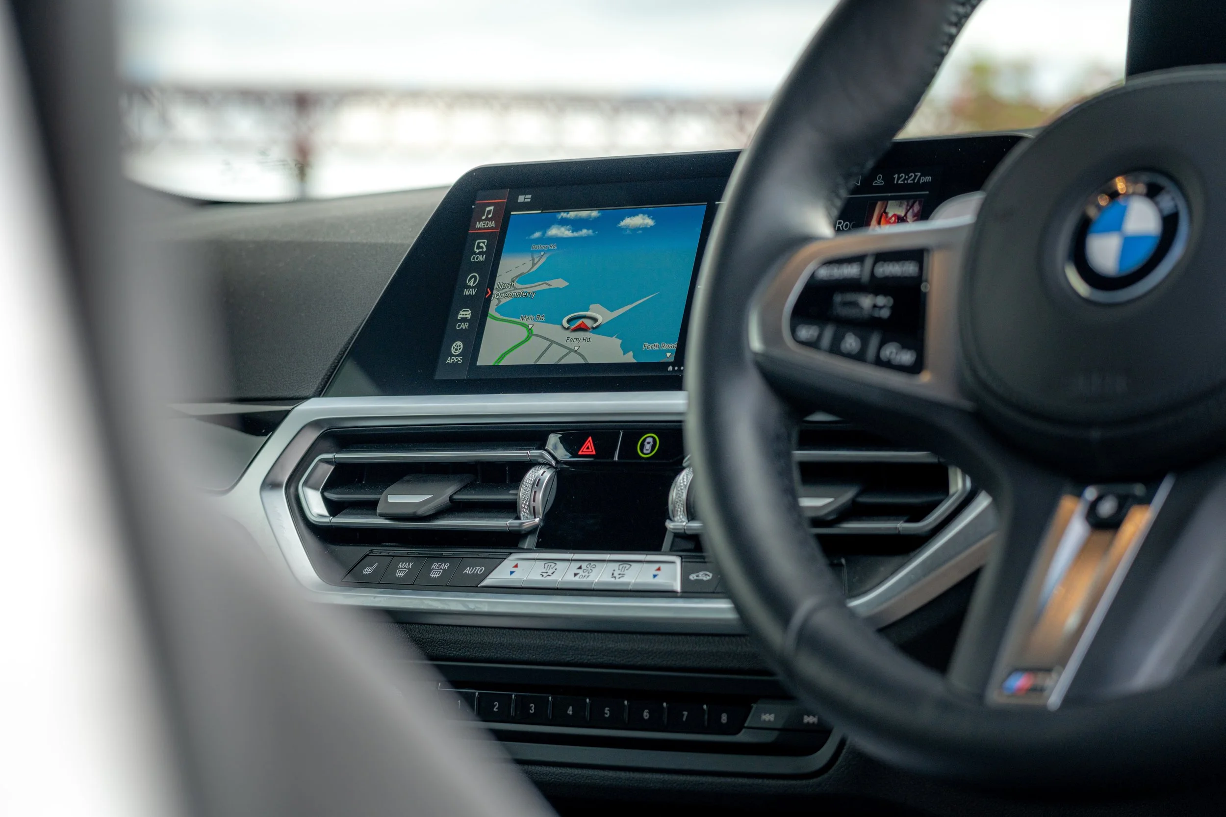 Car interior showing dashboard with navigation screen displaying a map and steering wheel with BMW logo.