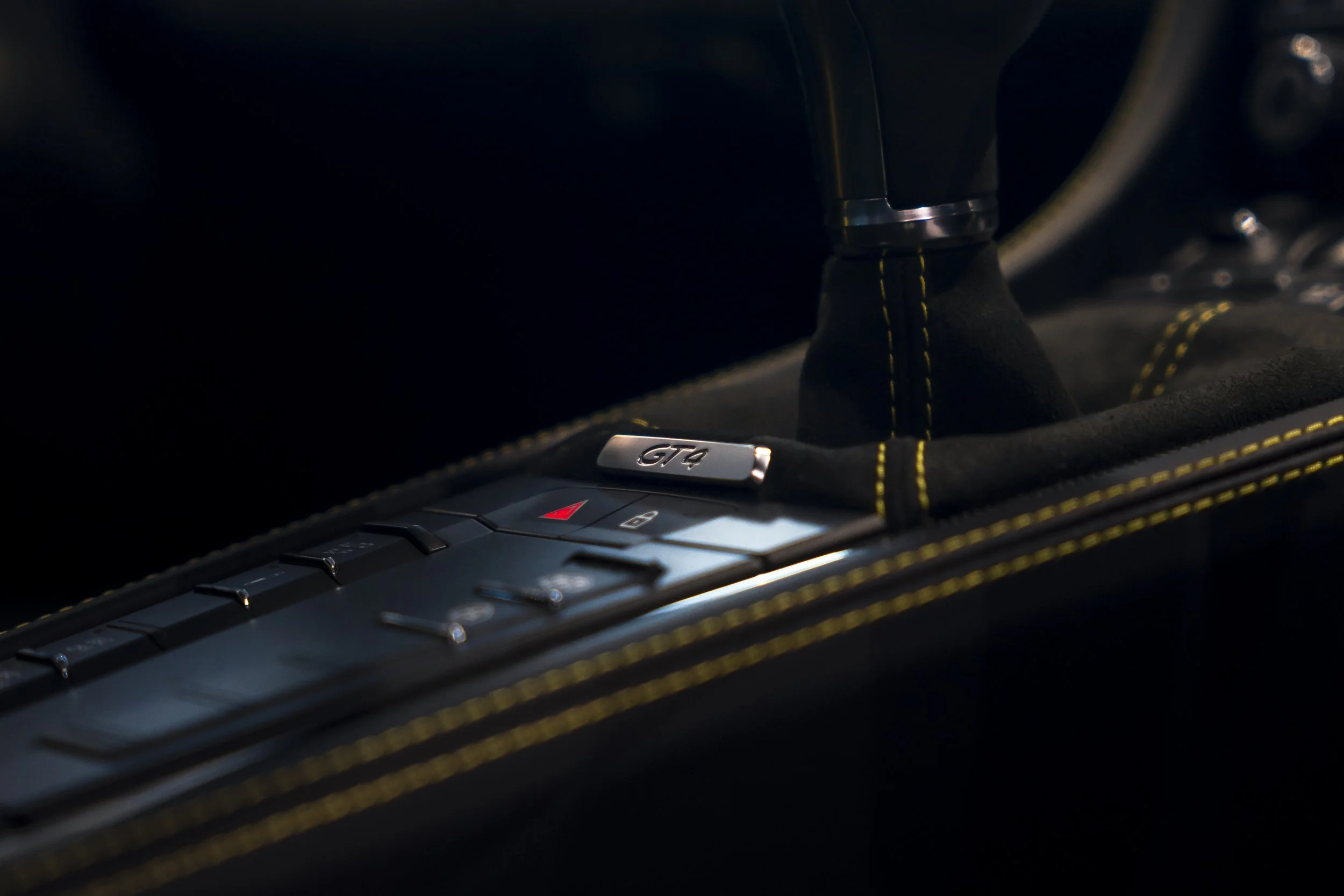 Close-up of a black car interior focusing on the gear shift with a metal plaque labeled 'GTR' and yellow stitching on the fabric around the gear shift area.