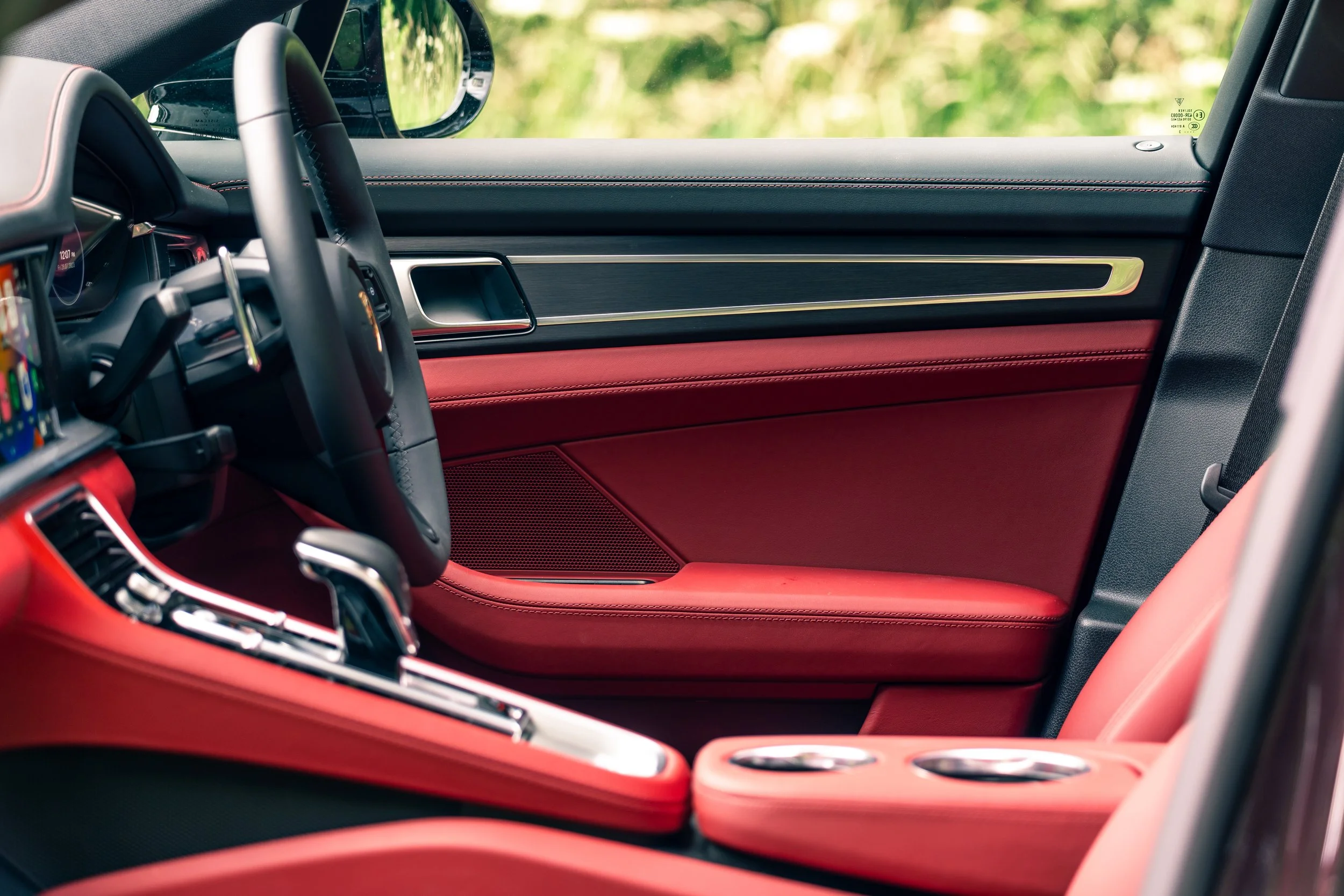Inside a luxury car with red leather seats, black dashboard, and modern controls, viewed through the driver's side window.