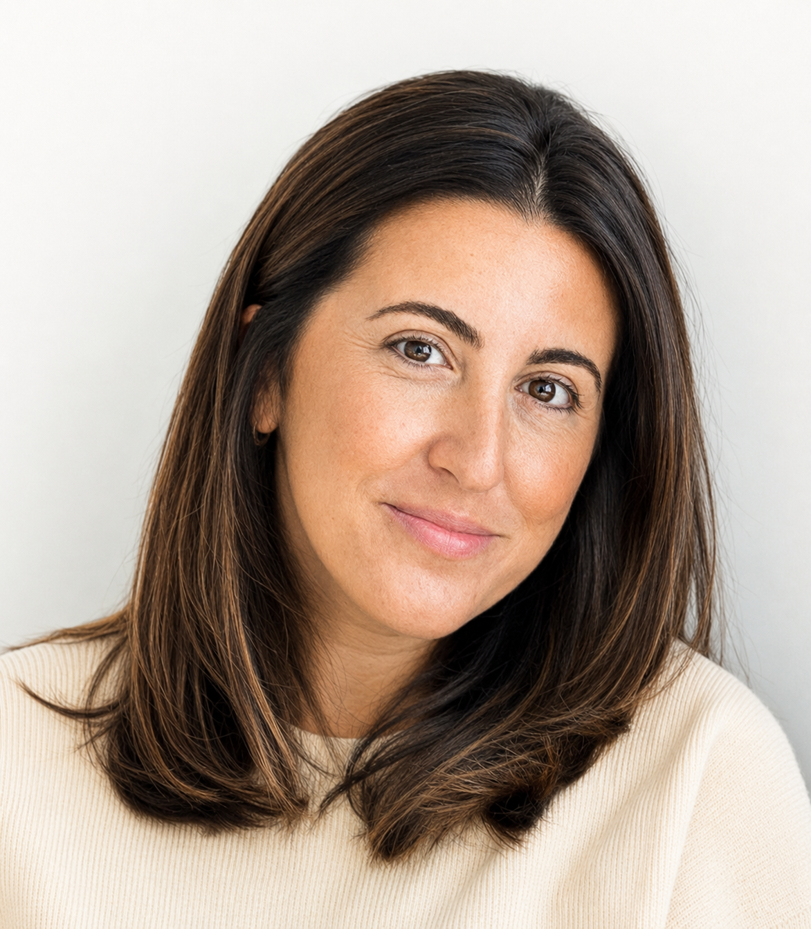 Portrait of a woman with shoulder-length brown hair, brown eyes, and a light beige top, smiling softly against a light background.