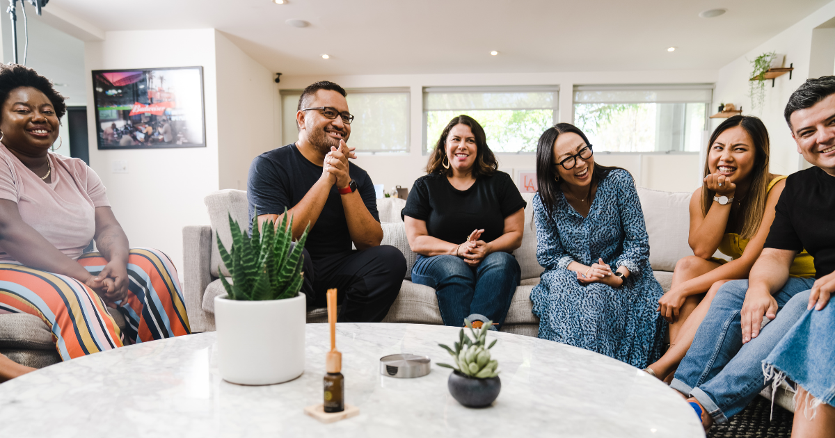 7 people sitting in a circle talking in a bright office.
