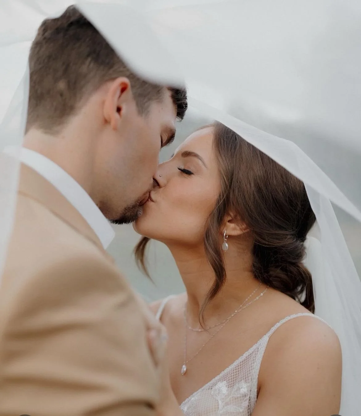 A couple sharing a kiss under a white veil on their wedding day.