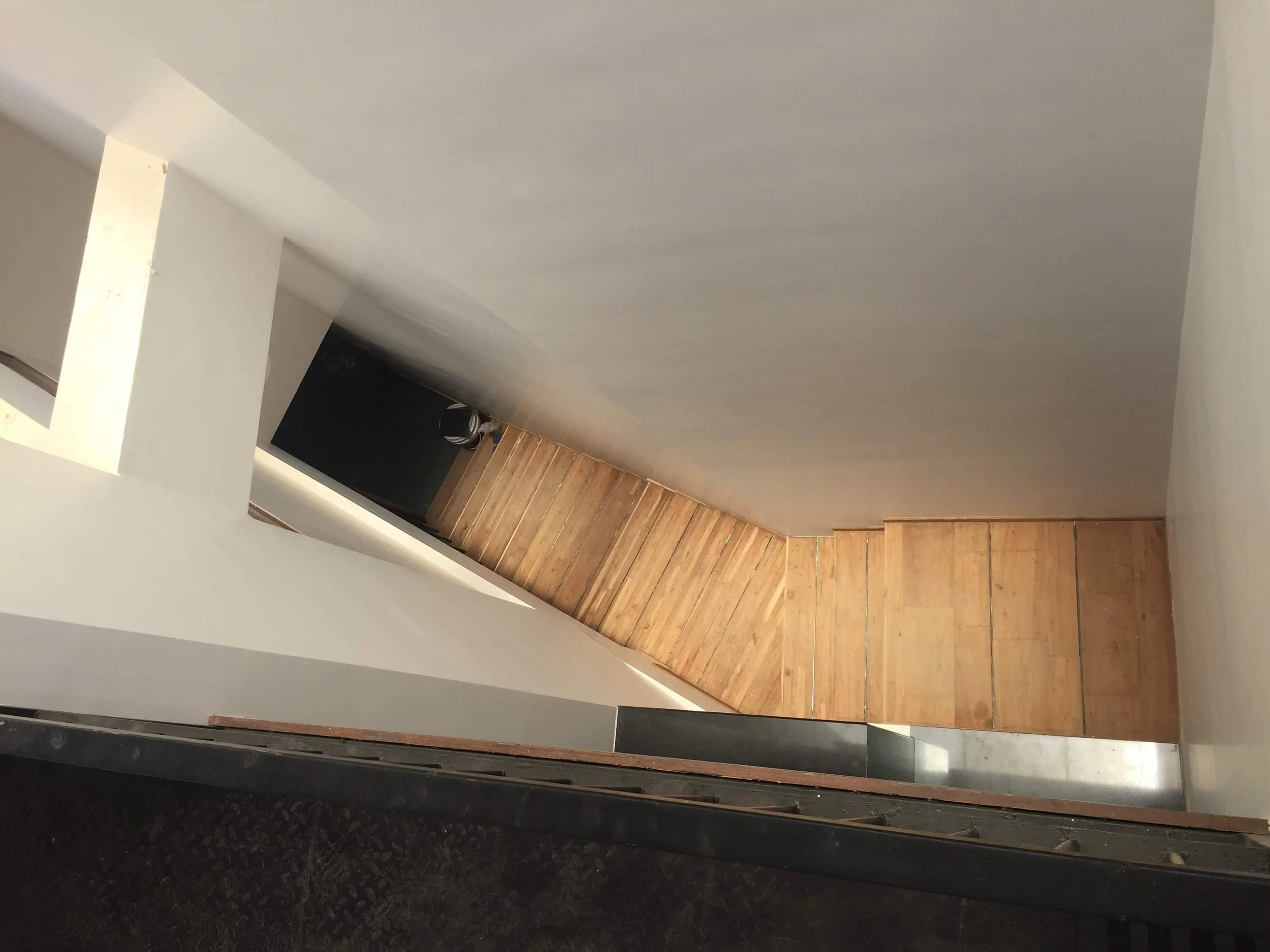 Looking down a staircase from above, showing wooden steps and a ledge with walls on either side.