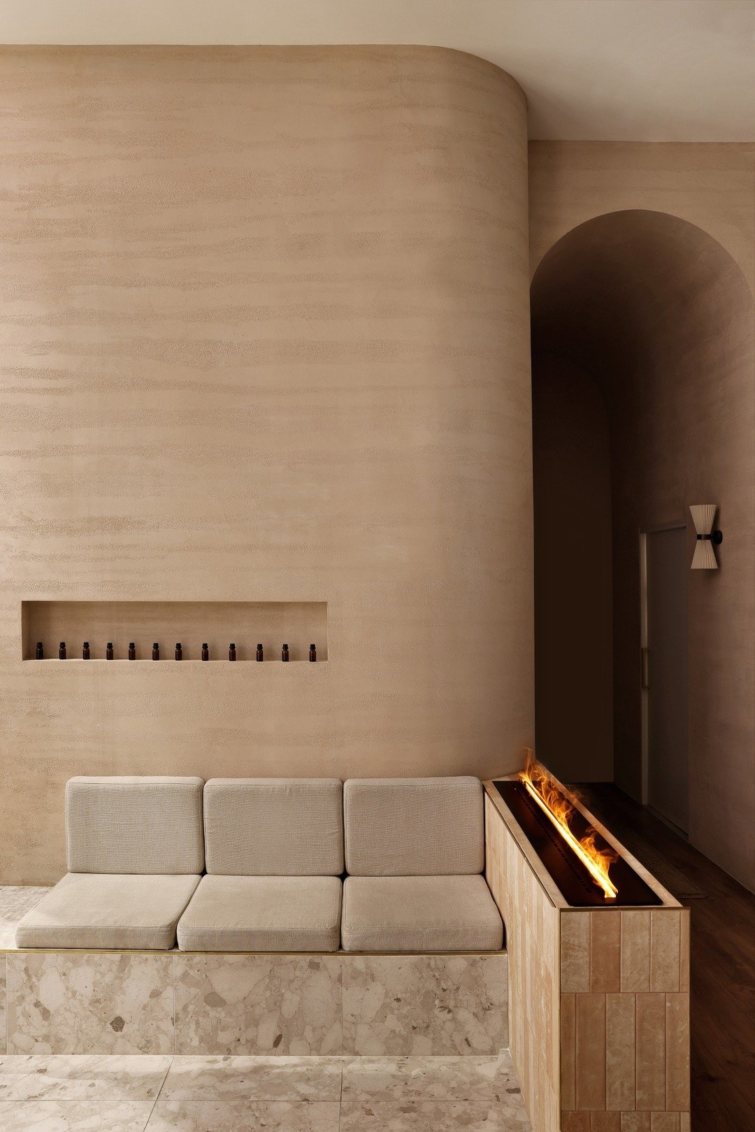 The waiting area features a built-in seat adjacent to an ambient fireplace at @ambiencewellness. Soothing nude-coloured travertino render, rich timber accents, and varied textures complete the grounding space.

Client / @ambiencewellness
Interior Des