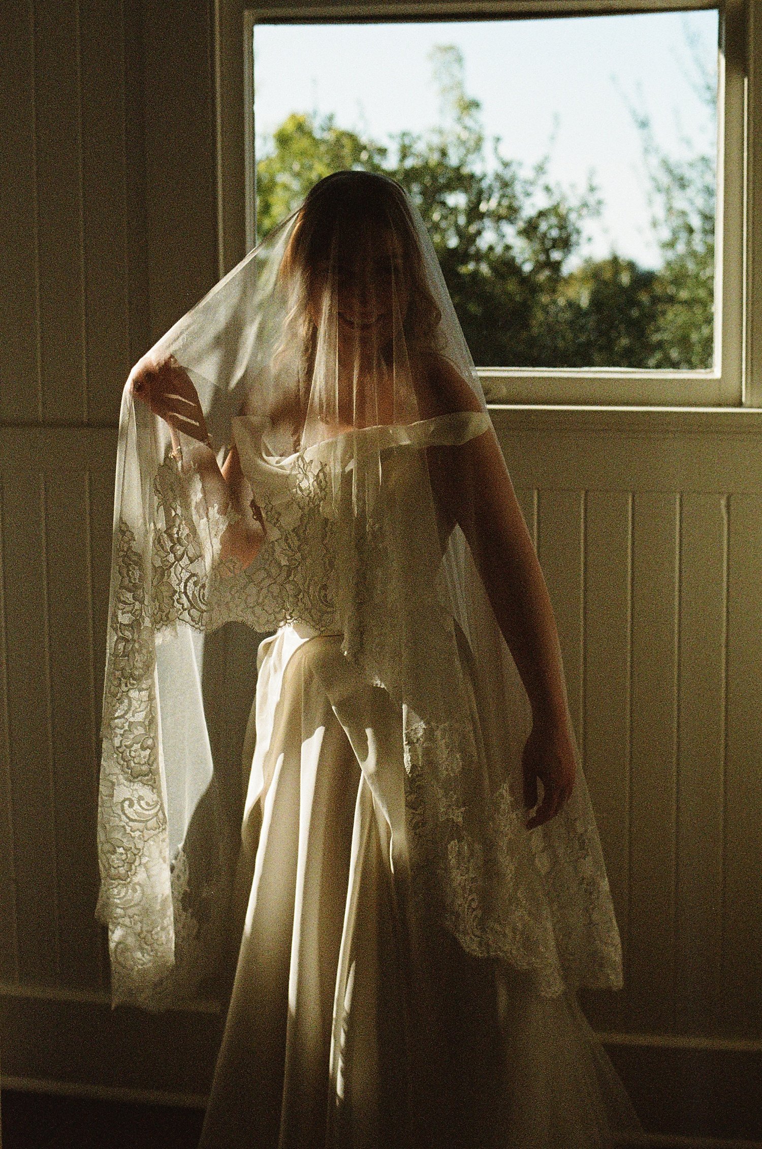  bride with long ornate veil stands near window by Jessica Joseph Photography 